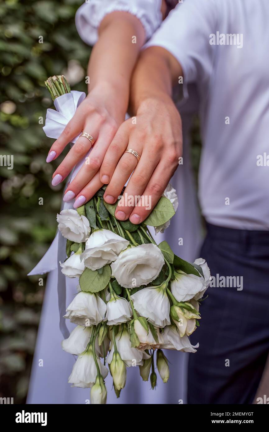 Goldringe an den Händen von Frischvermählten aus nächster Nähe. Gut gepflegte Hände und Finger der Frischvermählten mit wunderschöner Maniküre. Hochzeitsblumen und Stockfoto
