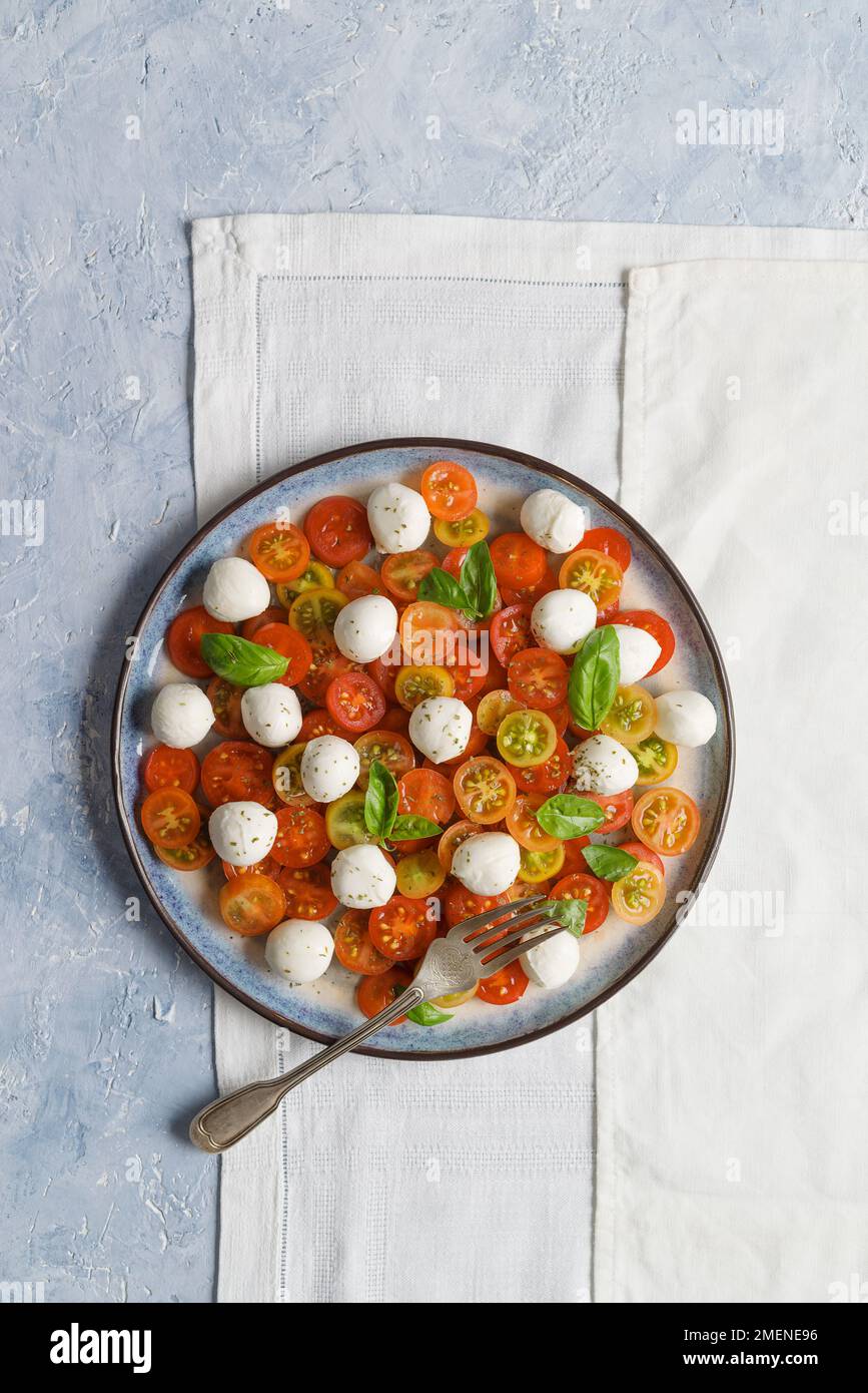 Isolierte Platte mit Tomatensalat mit Thunfisch, Mozzarella-Kirschen und Basilikumblättern. Flach verlegt. Speicherplatz kopieren. Stockfoto