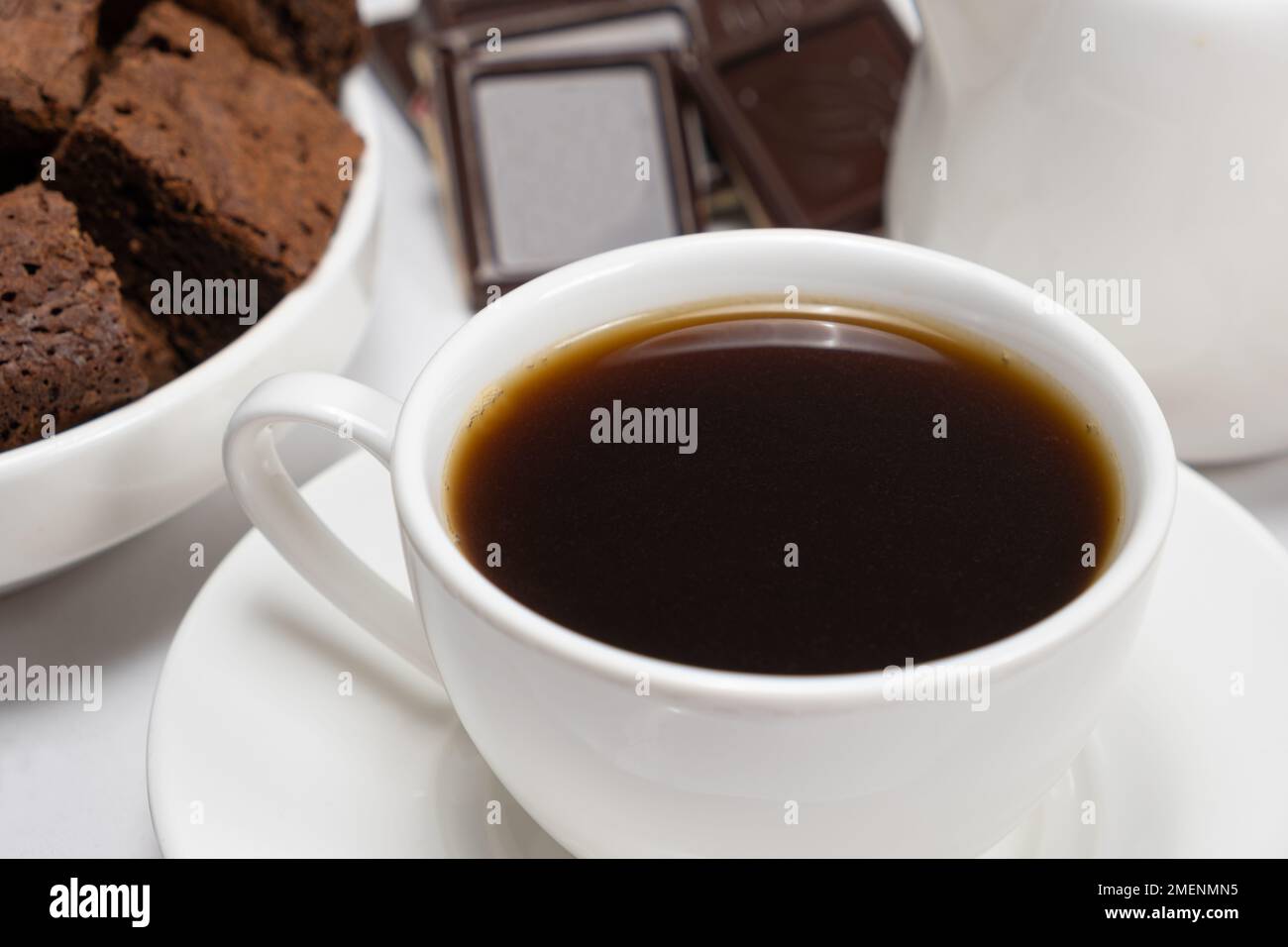 Nahaufnahme von Kaffee in einer Tasse, Schokoladenkuchen und Schokoladenstückchen auf weißem Hintergrund Stockfoto