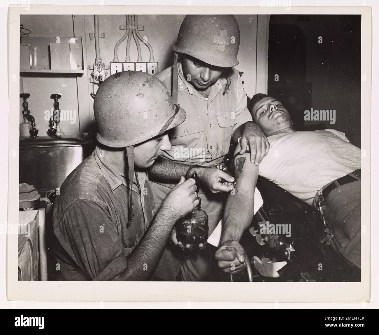 Der Coast Guardsman Albert W. Dill und der Public Health Chirurg Paul A. Kaufman spenden Blut an Bord eines von der Küstenwache bemannten Angriffstransports, um eine konstante Versorgung der Opfer der Saipan Invasion zu gewährleisten. Die Blutzufuhr war entscheidend, um die Marine während des Angriffs zu unterstützen. Stockfoto