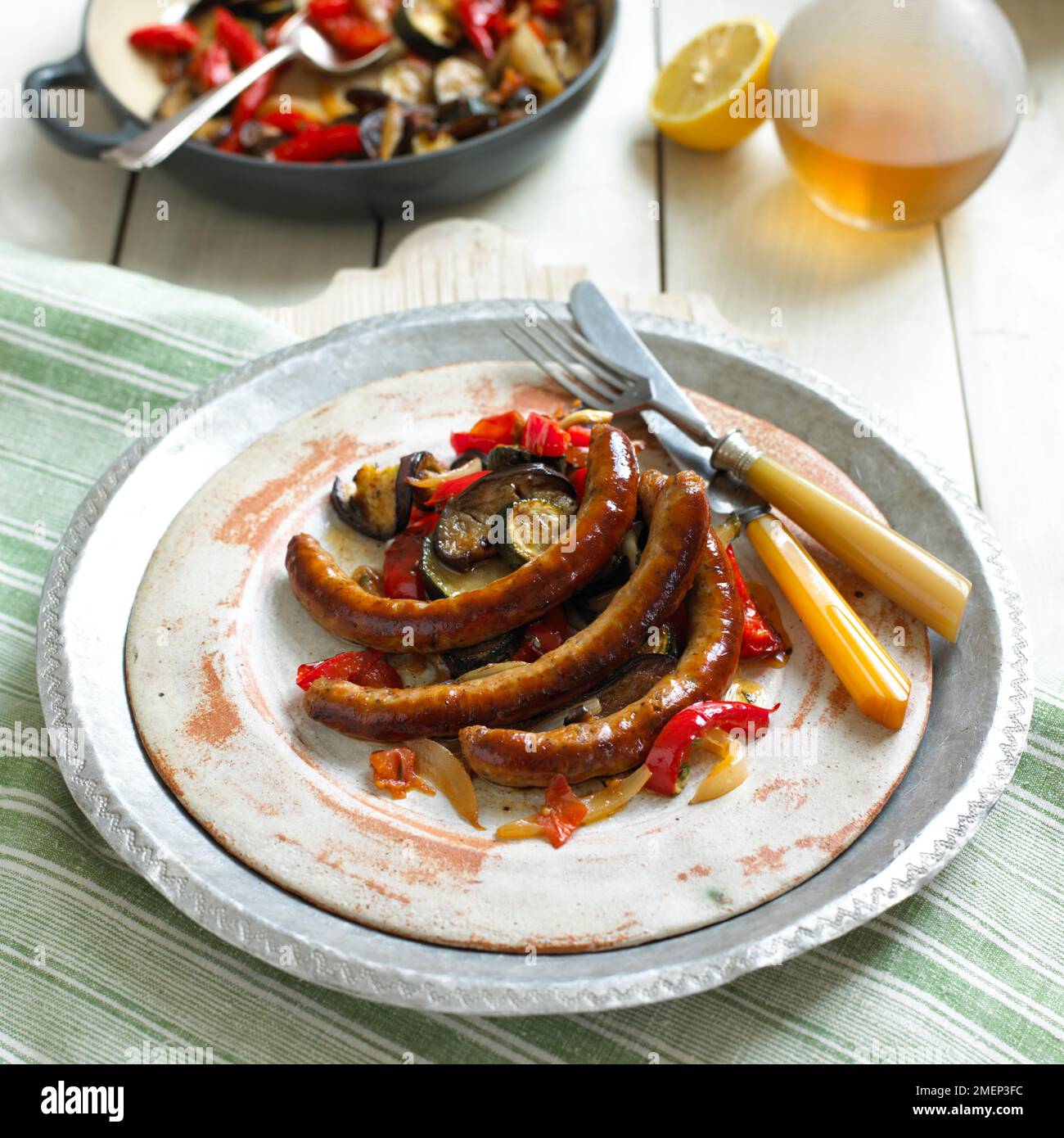 Gegrillter Merguez mit Ratatouille, serviert auf rustikalem Teller mit gekreuztem Besteck Stockfoto