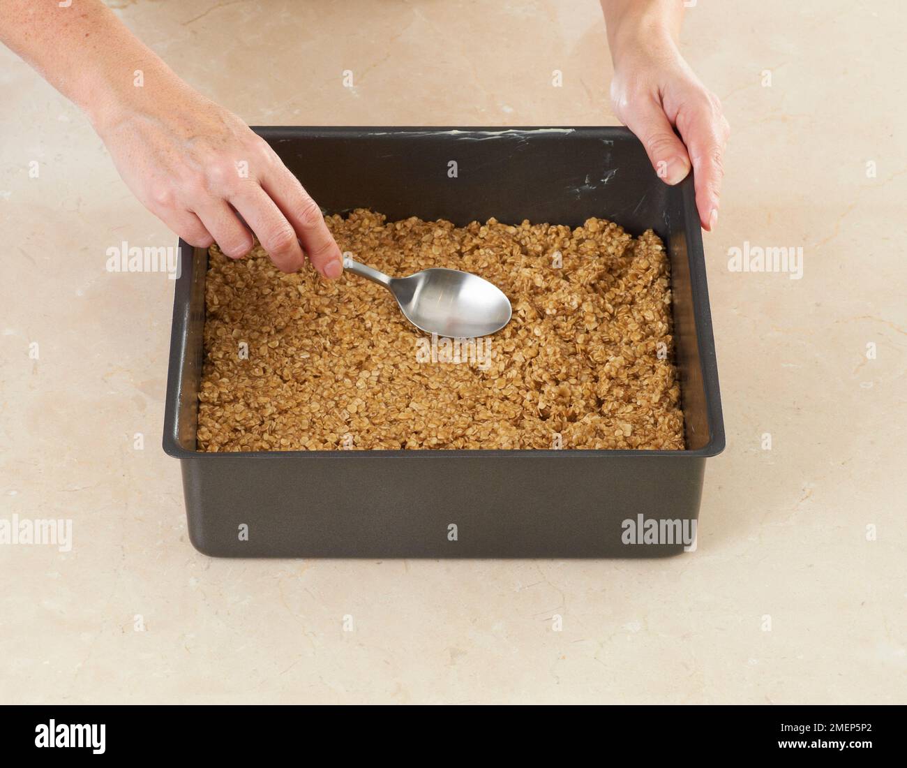 Mit dem Löffel die Flapjack-Mischung in der Backform abflachen Stockfoto