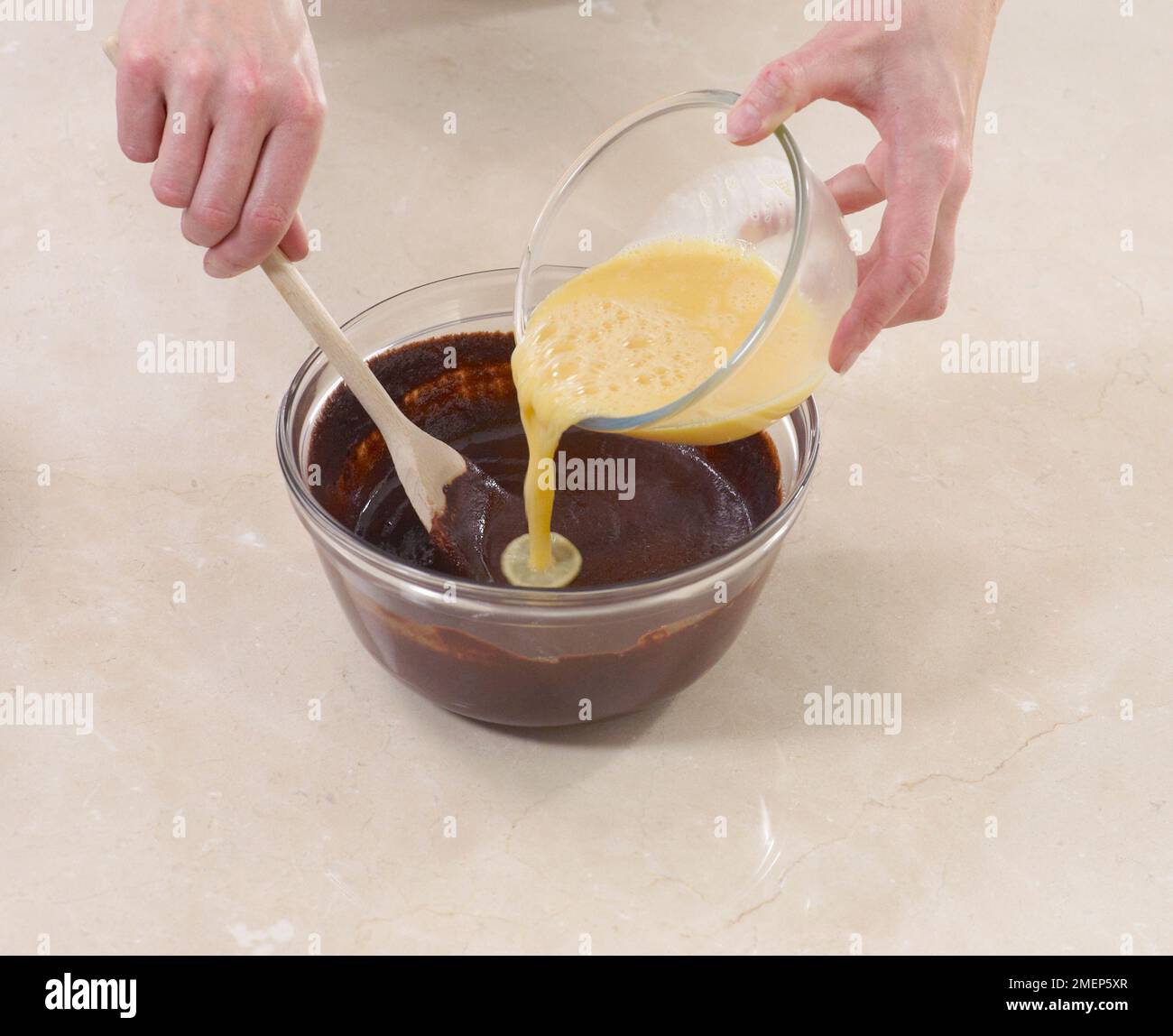 Brownies machen, Eiermischung in geschmolzene Schokolade gießen und mischen Stockfoto