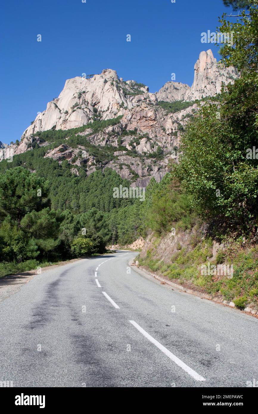 Frankreich, Korsika, La Route de Bavella - Blick entlang der Route mit den Felsformationen im Hintergrund, Les Aiguilles de Bavella Stockfoto