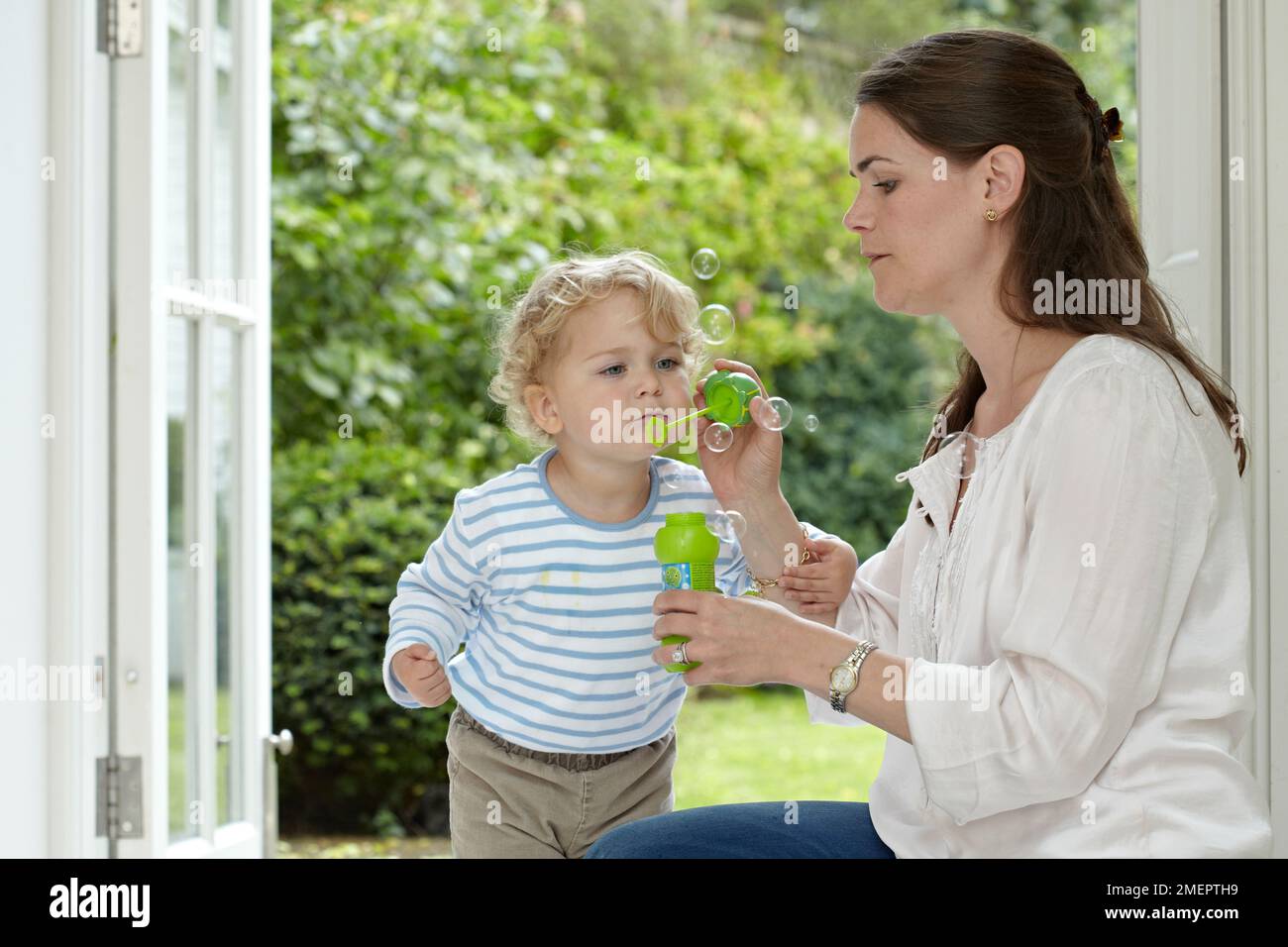 Ein Junge bläst einen Blasenstab, gehalten von einer Frau, 2 Jahre, 4 Monate Stockfoto