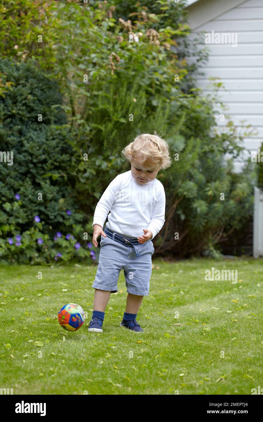 Ein Junge tritt einen Ball in einem Garten, 2 Jahre, 4 Monate Stockfoto