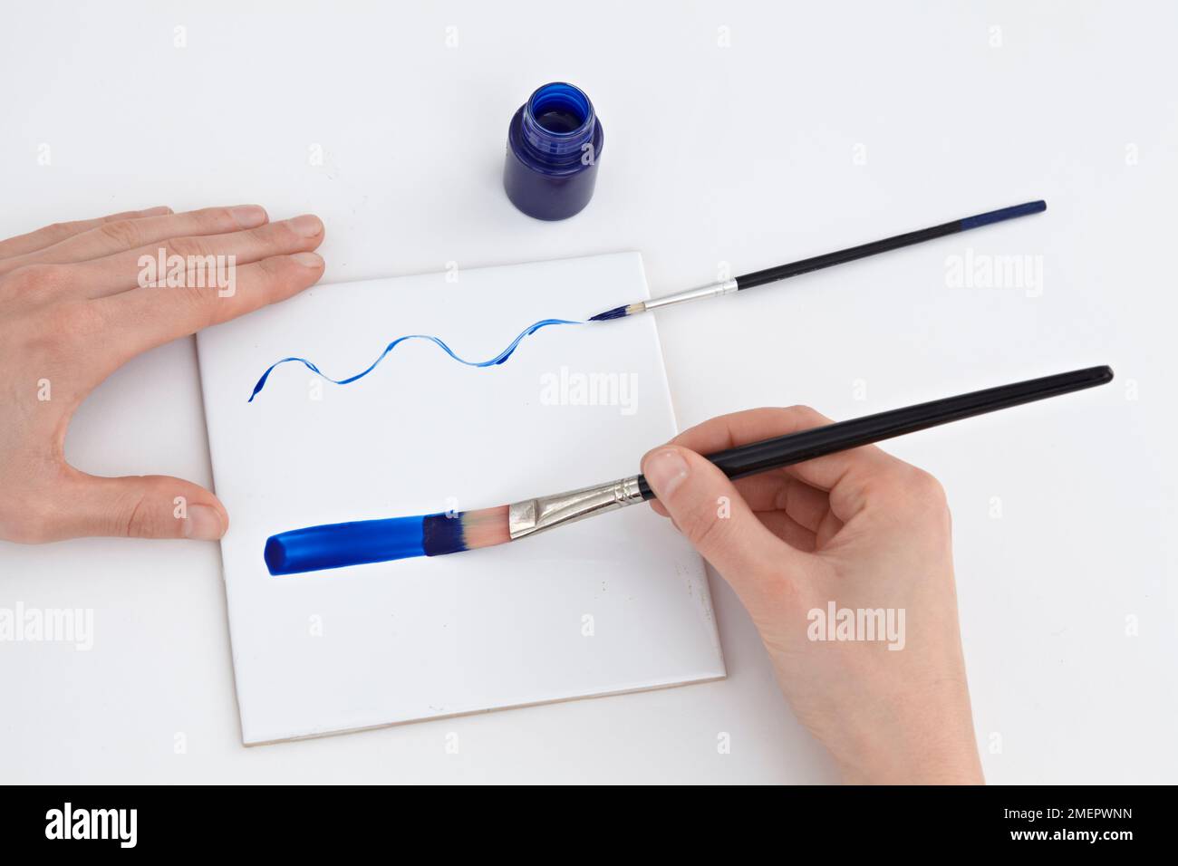 Verwendung von blauer Keramikfarbe auf Fliesen zum Experimentieren mit verschiedenen Pinseln, Nahaufnahme Stockfoto