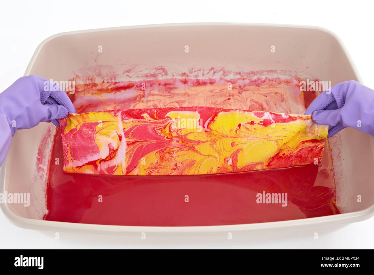 Halten Sie zwei Ecken des Stoffes schnell nach oben, damit überschüssiges Wasser und marmorierende Tinte abtropfen können, Nahaufnahmen Stockfoto