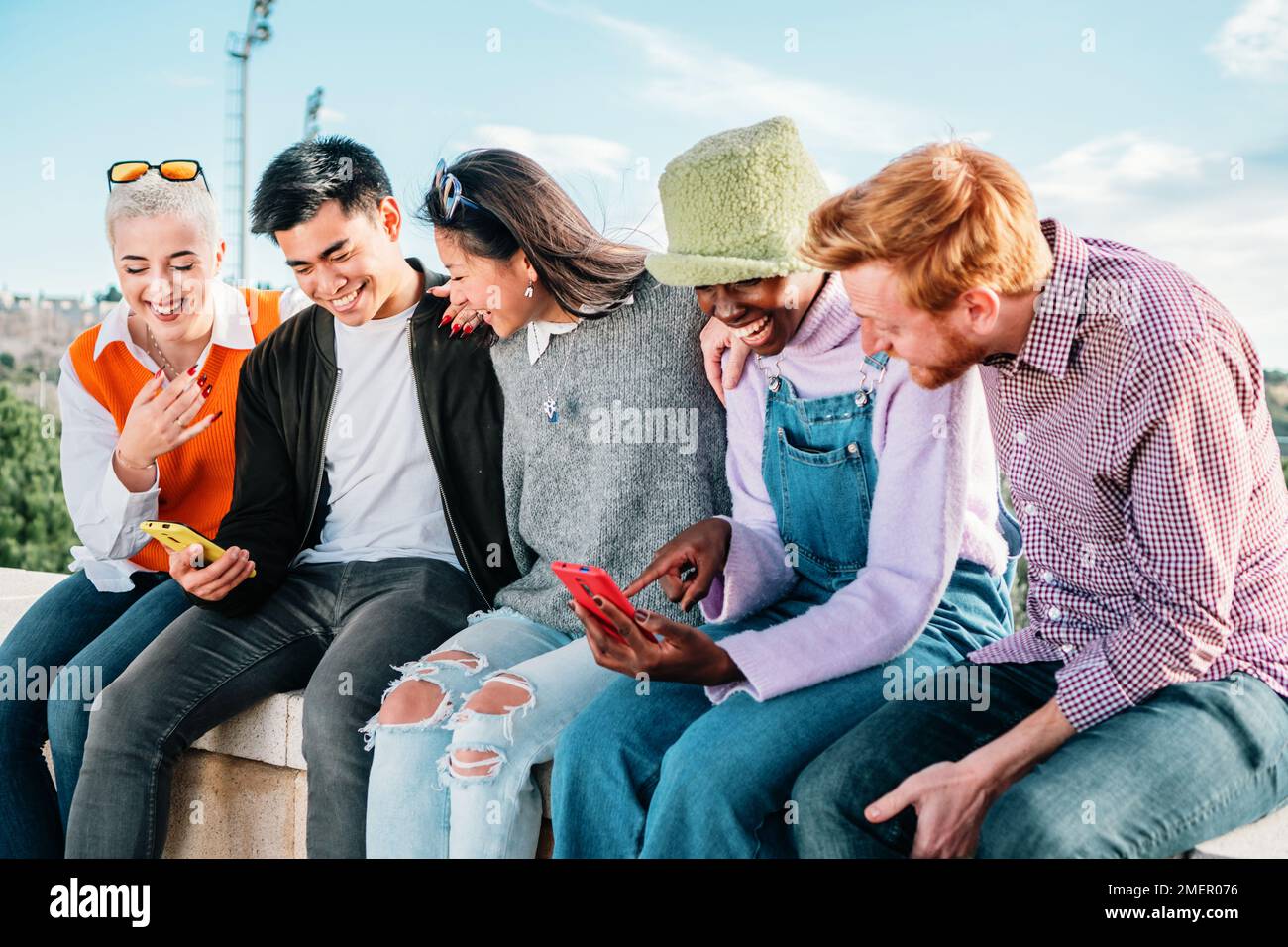 Fünf multiethnische Freunde schauen sich Videos in sozialen Medien an, sitzen zusammen und haben Spaß. Hochwertiges Foto Stockfoto