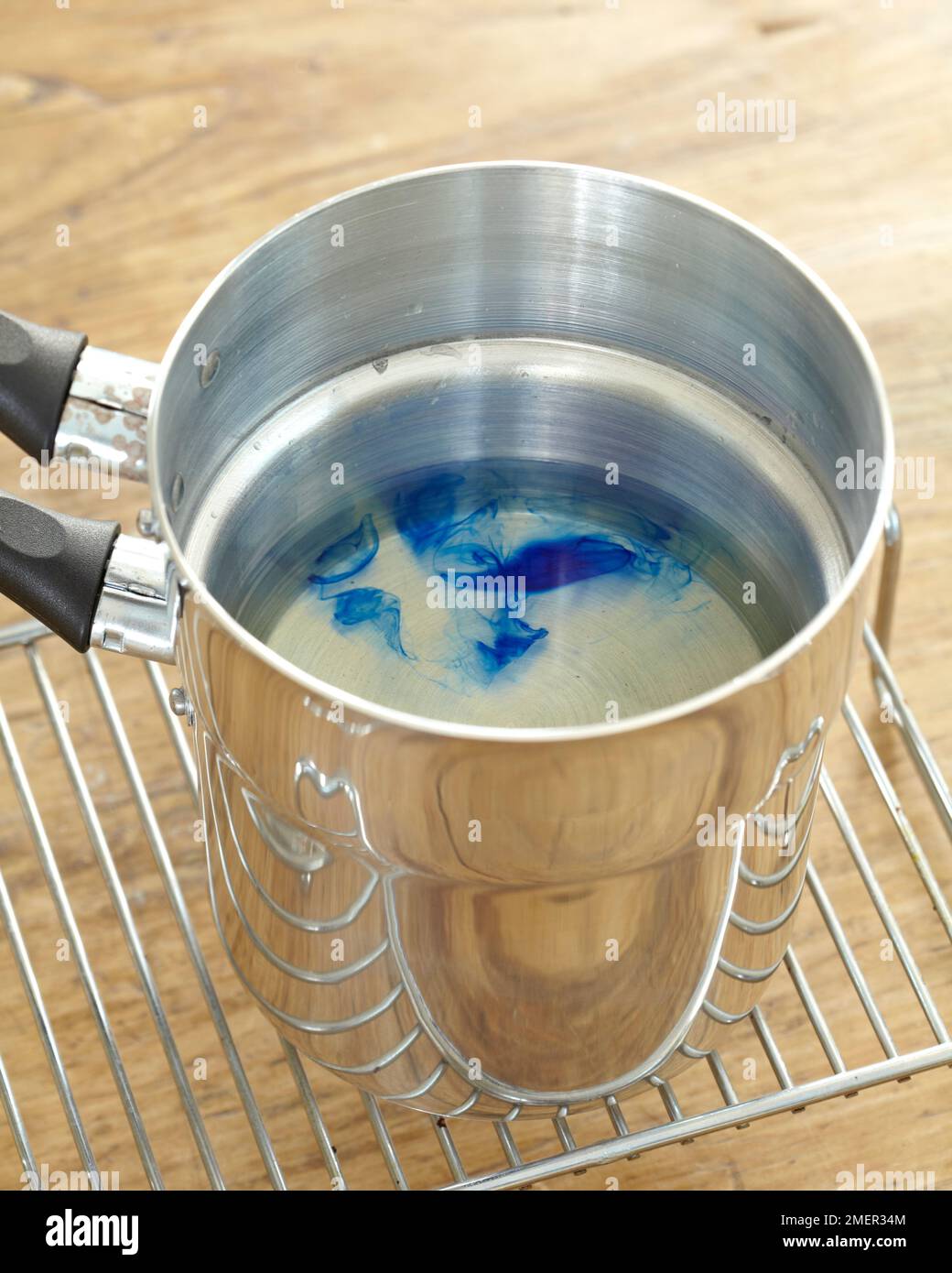 Blauer Farbstoff, der sich am Boden des Doppelkessels in Wasser auflöst (Herstellung von Kerzen) Stockfoto