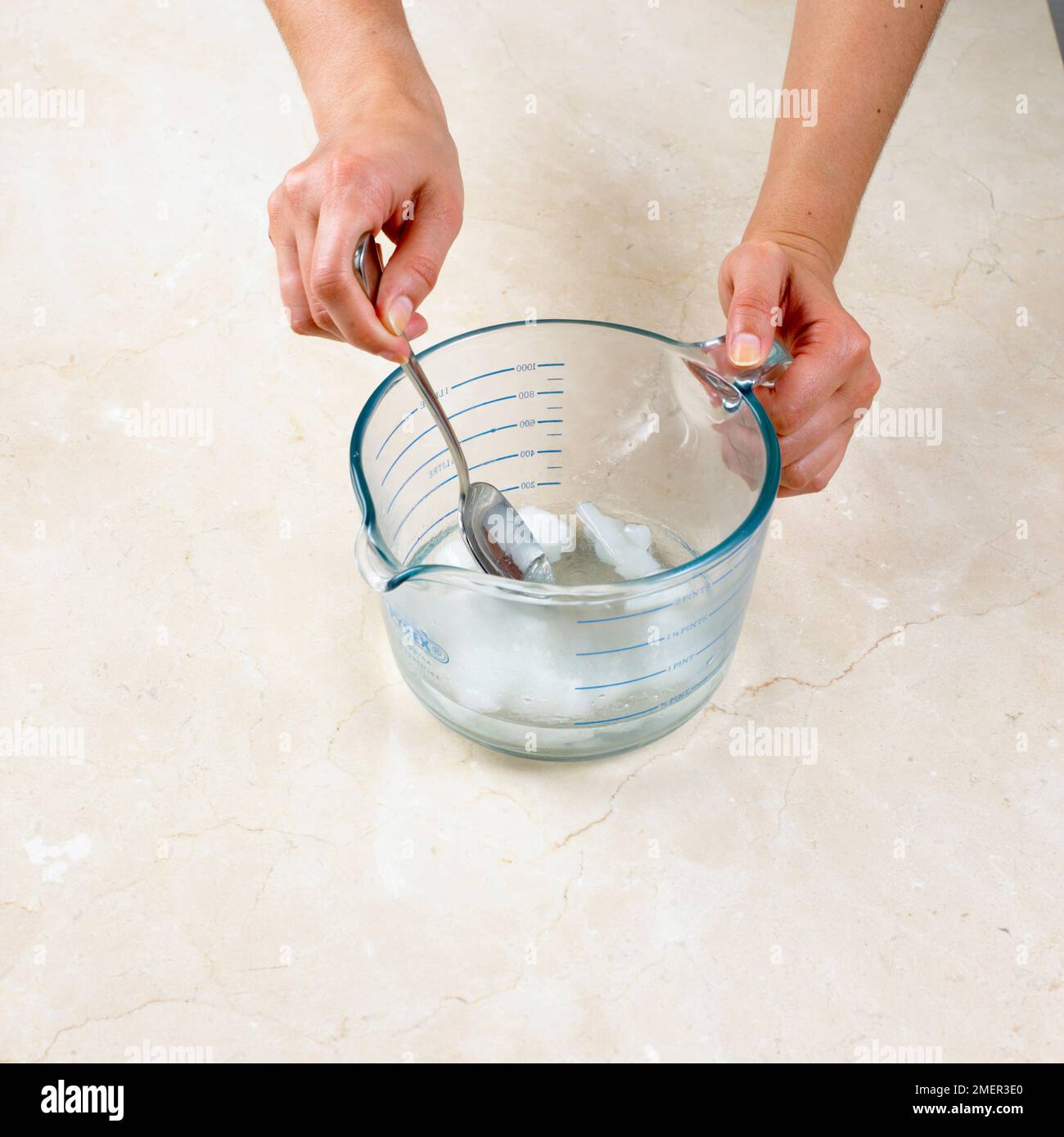 Zubereitung von Heißwasserkrustengebäck, Zugabe von gewürfeltem Schmalz zu gekochtem Wasser in der Kanne und Rühren der Mischung mit einem Metalllöffel, bis das Fett geschmolzen ist Stockfoto