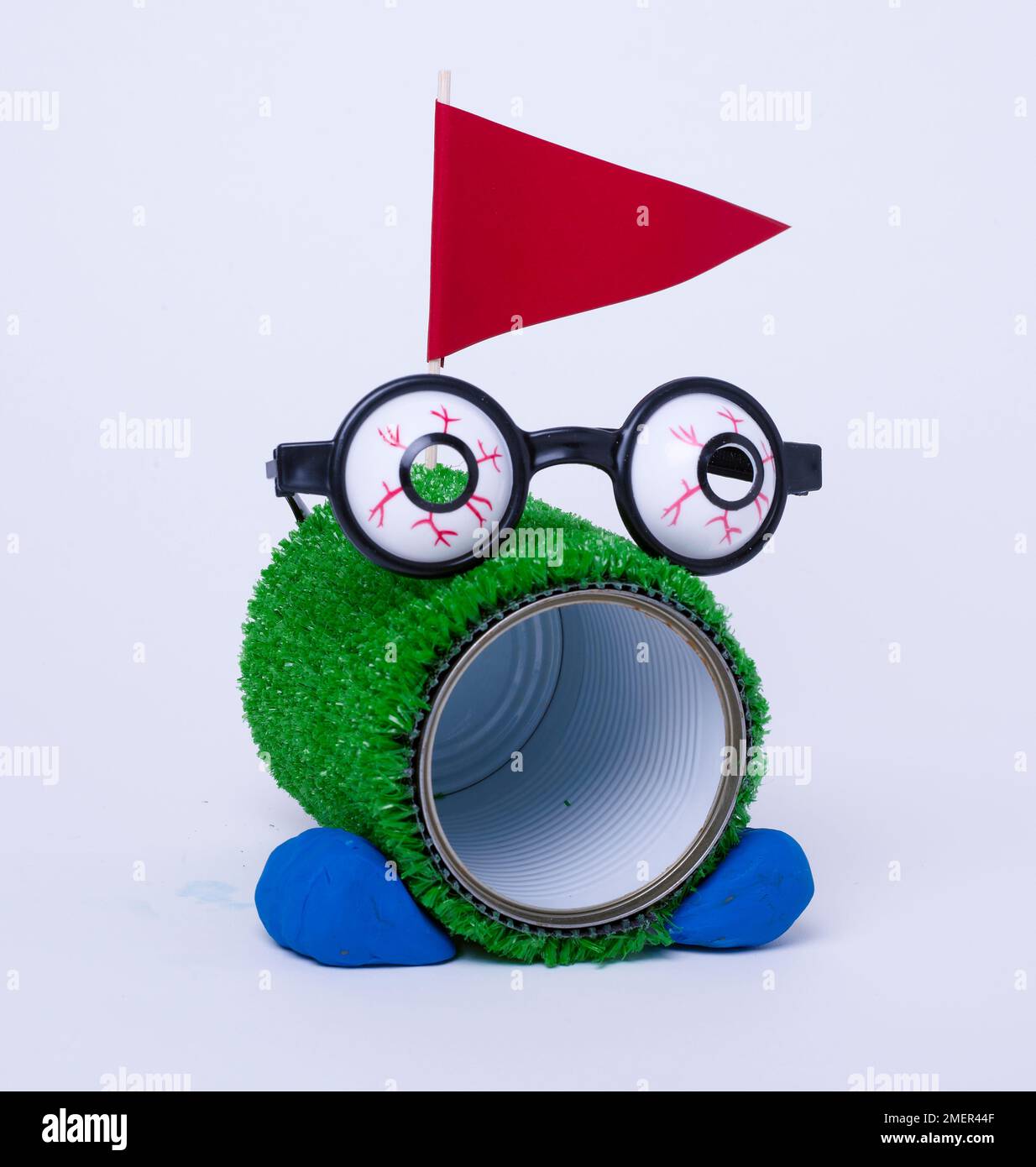 Golfloch, Blechdose in Astro-Rasen eingewickelt, Googly-Brille, Füße und Flagge Stockfoto