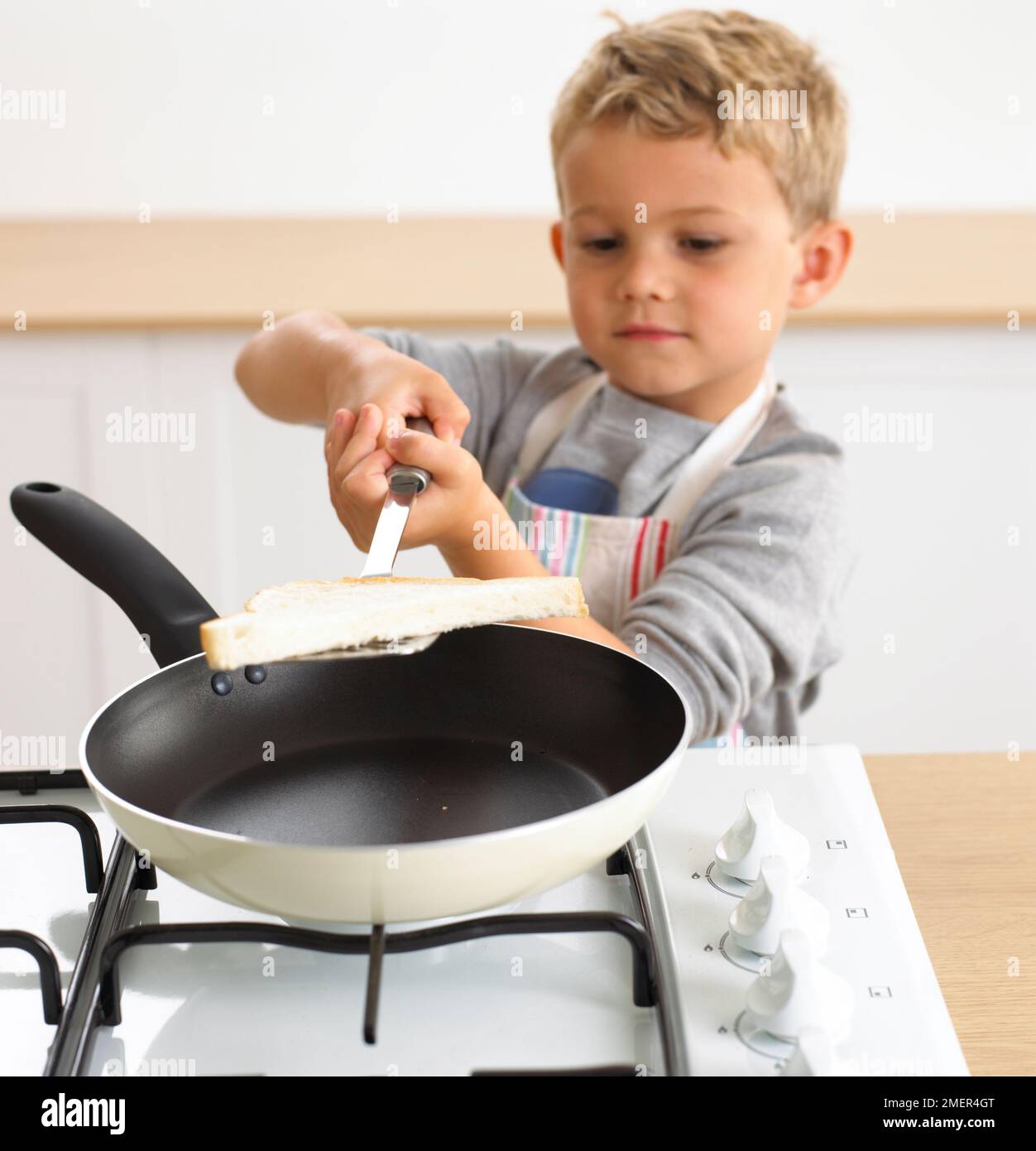 Ein Junge, der Eierbrot in die Bratpfanne steckte, 4 Jahre Stockfoto