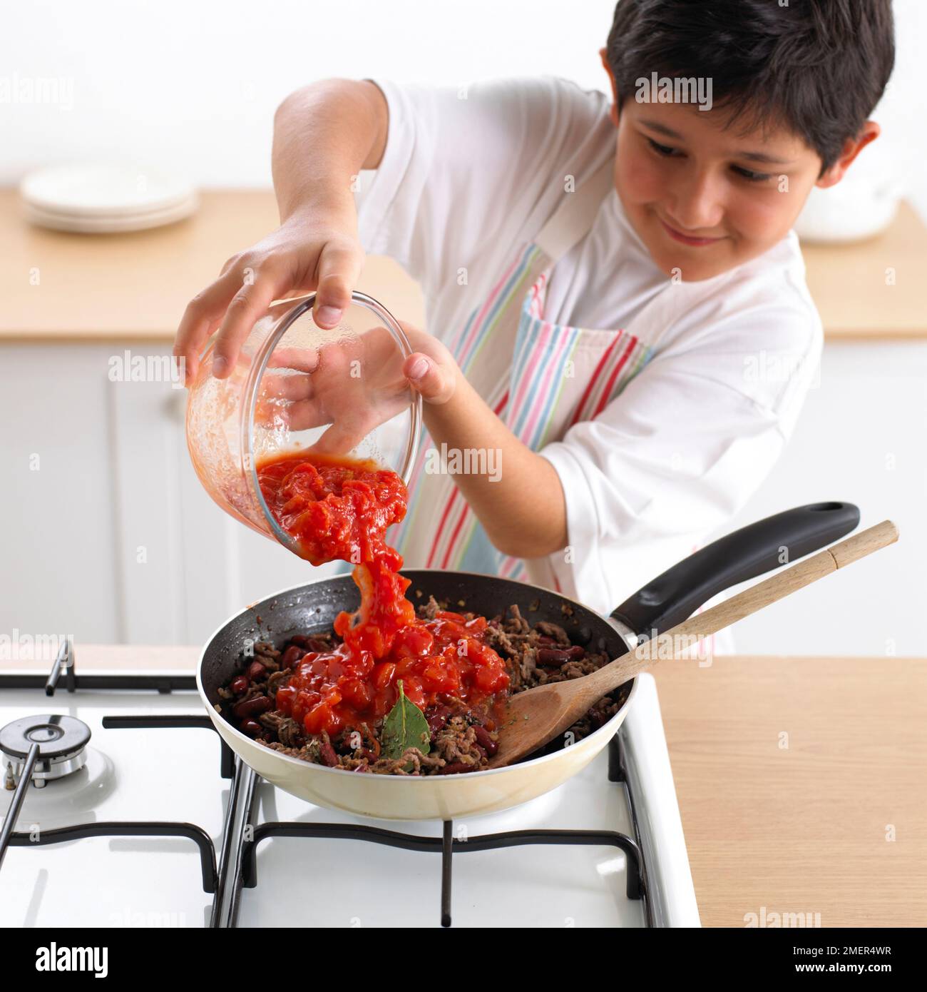 Junge, der gebratenes Hackfleisch mit geschnittenen Tomaten serviert, 9 Jahre Stockfoto