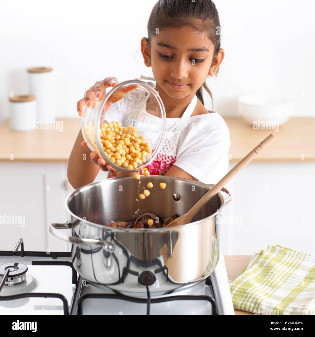 Ein Mädchen, das Kichererbsen zu einem Kochtopf hinzufügt, 8 Jahre Stockfoto