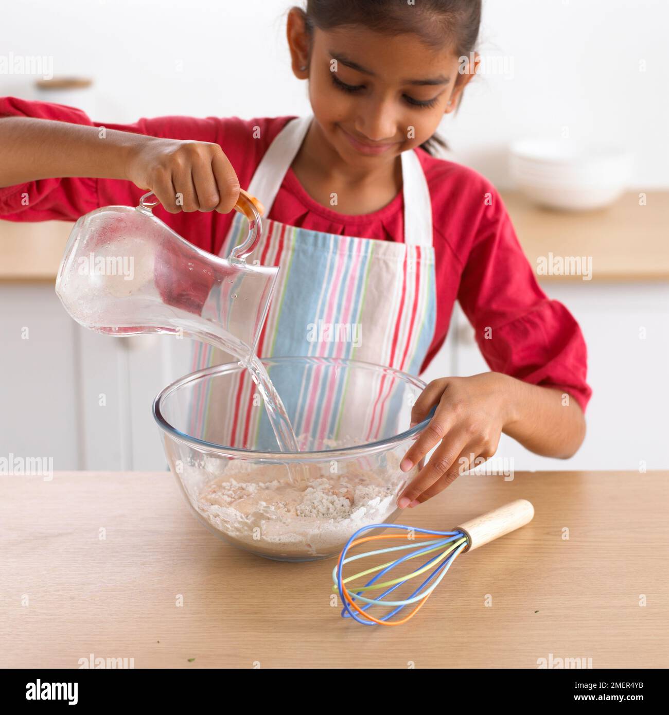 Ein Mädchen, das Wasser in eine Mehlschüssel gießt, 8 Jahre Stockfoto Ein Mädchen, das Wasser in eine Mehlschüssel gießt, 8 Jahre Stockfoto