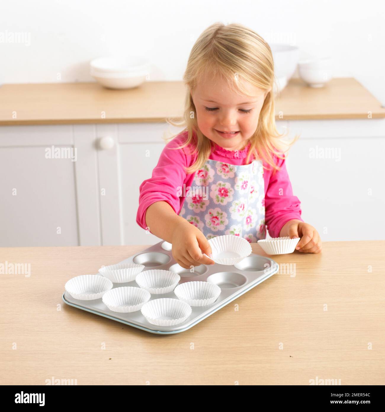 Ein Mädchen, das Kuchenbehälter auf Kuchenform legt, 3 Jahre Stockfoto