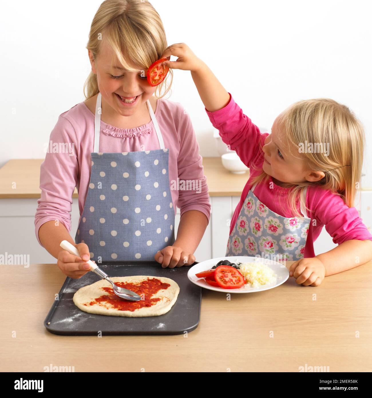 Zwei Mädchen, Topping auf rohe pizza Base, 7 und 3 Jahre. Stockfoto