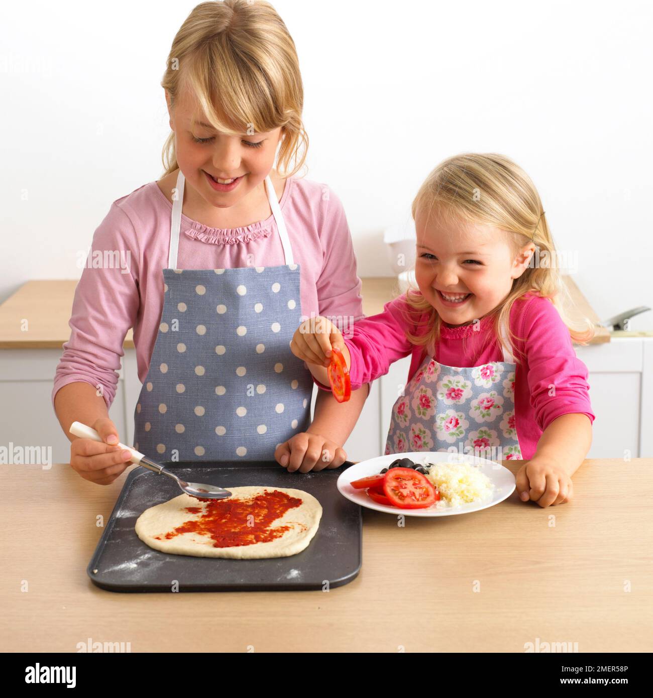 Zwei Mädchen, Topping auf rohe pizza Base, 7 und 3 Jahre. Stockfoto