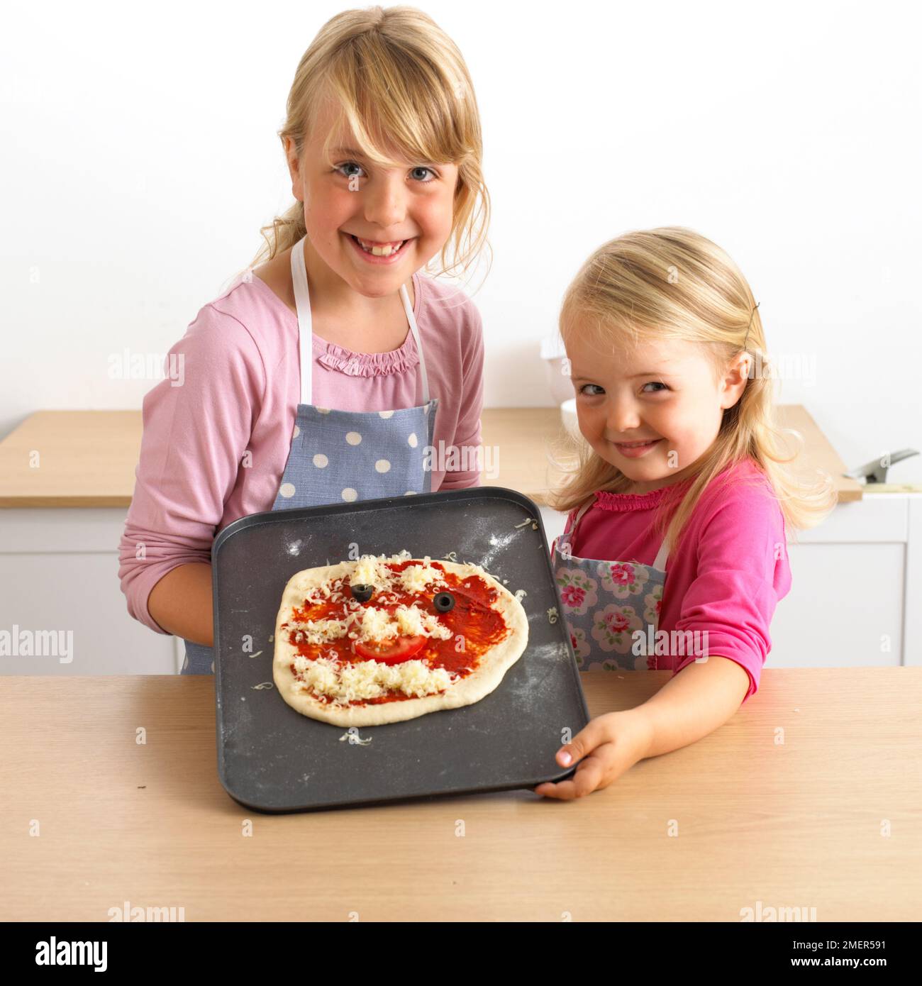 Zwei Mädchen mit einem Backblech mit ungekochter Pizza, 7 und 3 Jahre alt Stockfoto