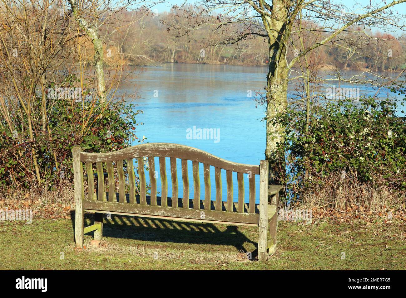 Eine hölzerne Bank am See mit einer schönen Aussicht durch die Bäume. Stockfoto