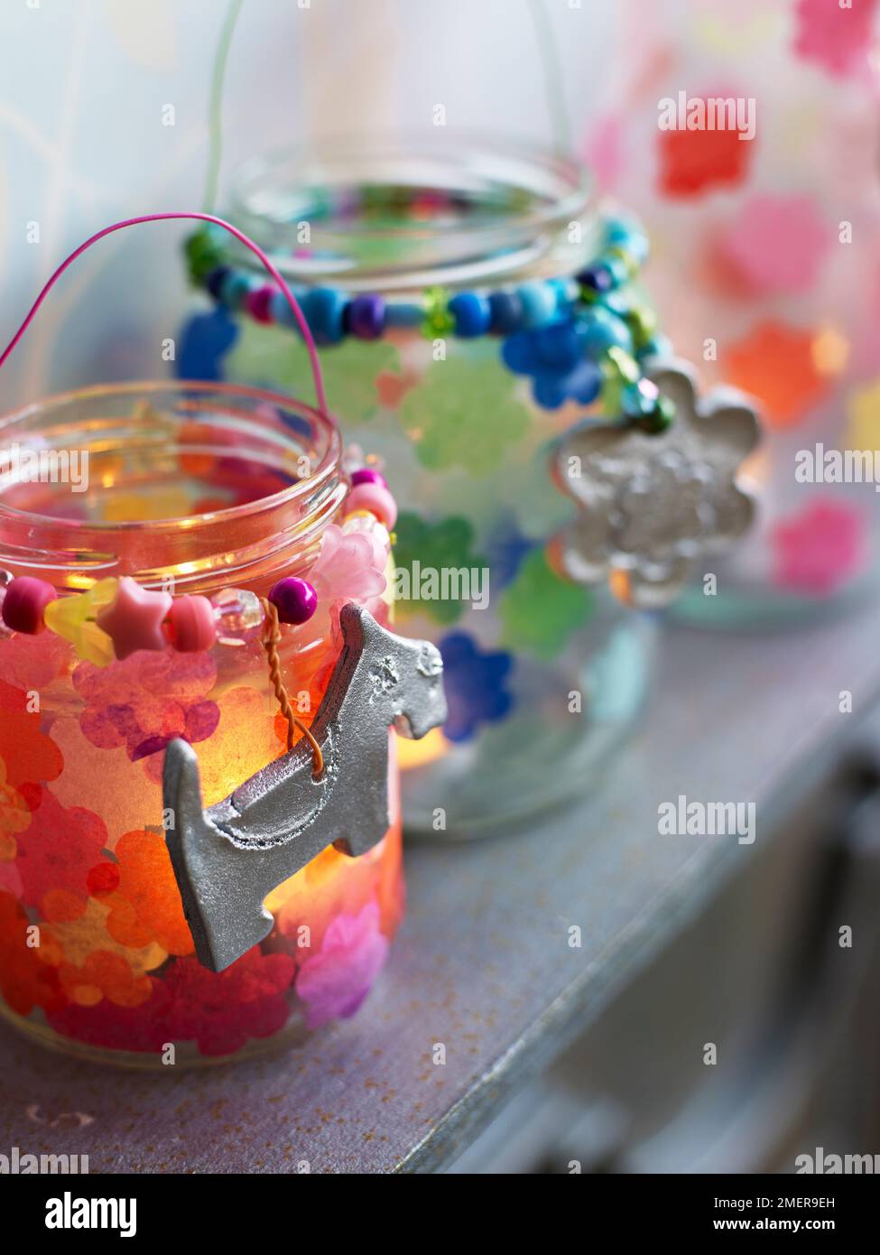 Gläser aus Kerzenglas mit Papiertaschenblumen und silbernen Anhängern auf dem Kaminsims Stockfoto