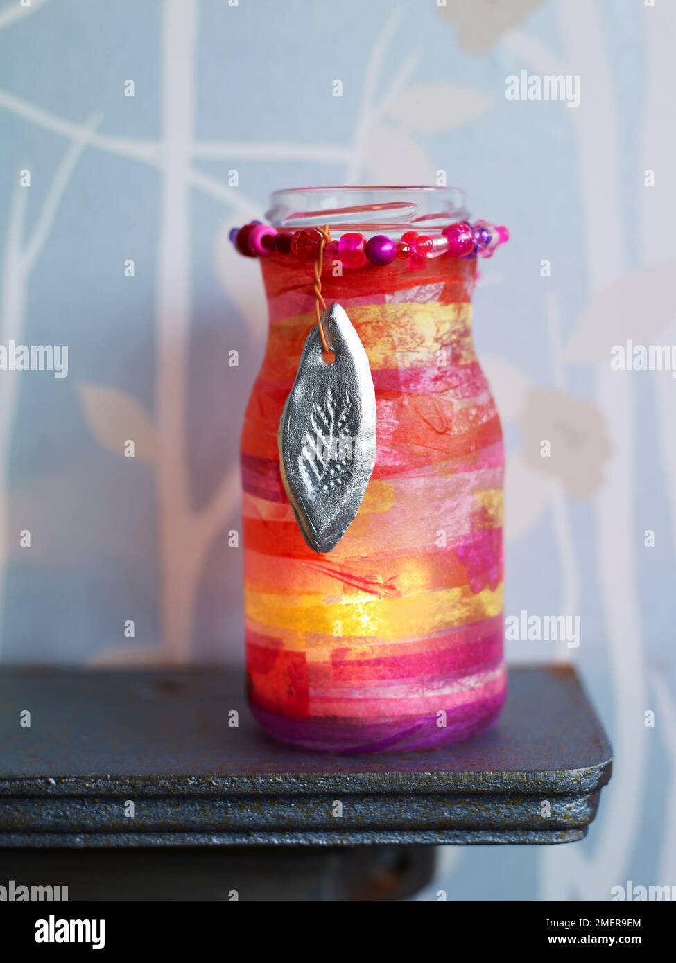 Gläser aus Kerzenglas mit Papiertaschenblumen und silbernen Anhängern auf dem Kaminsims Stockfoto