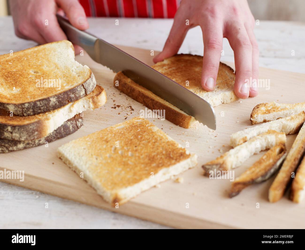 Ein Sandwich, das die Krusten von Scheiben getoasteten Weißbrots schneidet Stockfoto