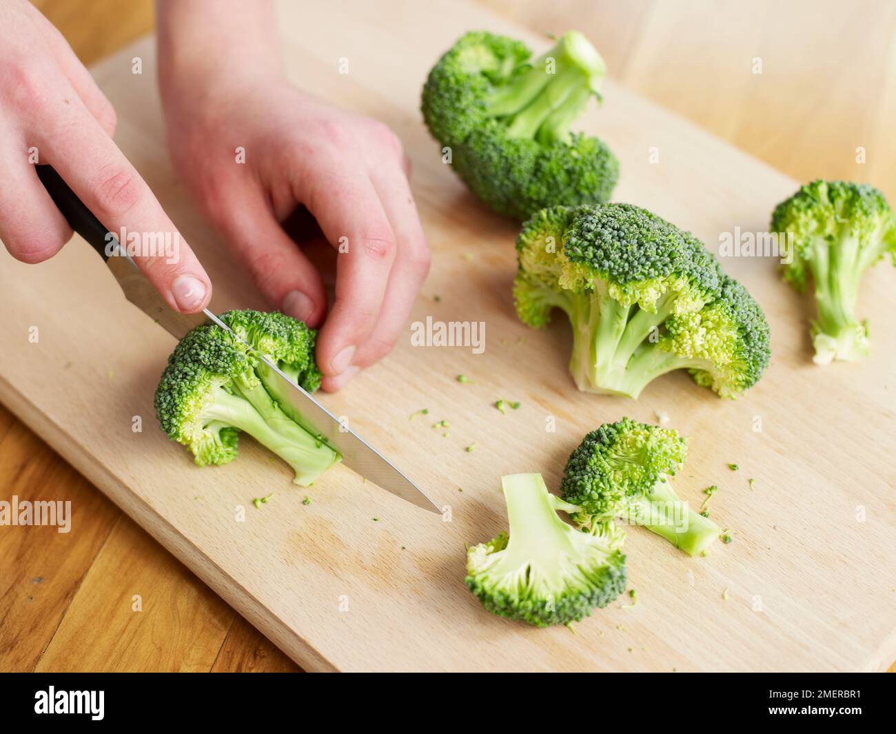Schneiden von rohem Brokkoli auf Holzbrett Stockfoto
