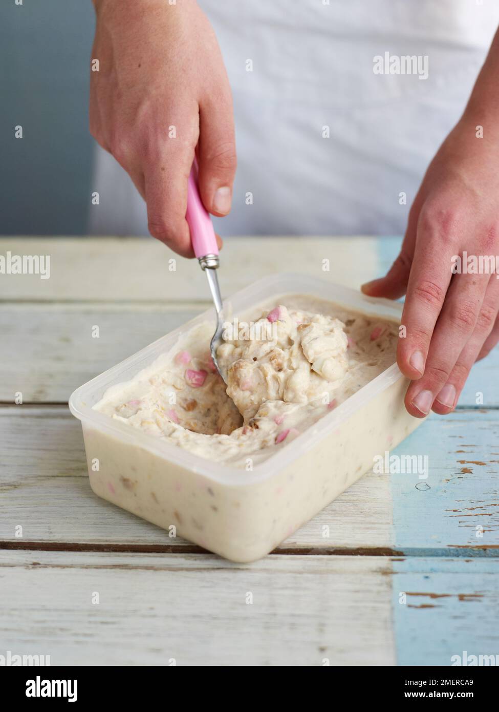 Zubereiten von gefrorenem Joghurt, Löffeln von Joghurt, Marshmallow, Schokoladenkeks und Fudge-Mischung in Kunststoffdosen zum Einfrieren Stockfoto