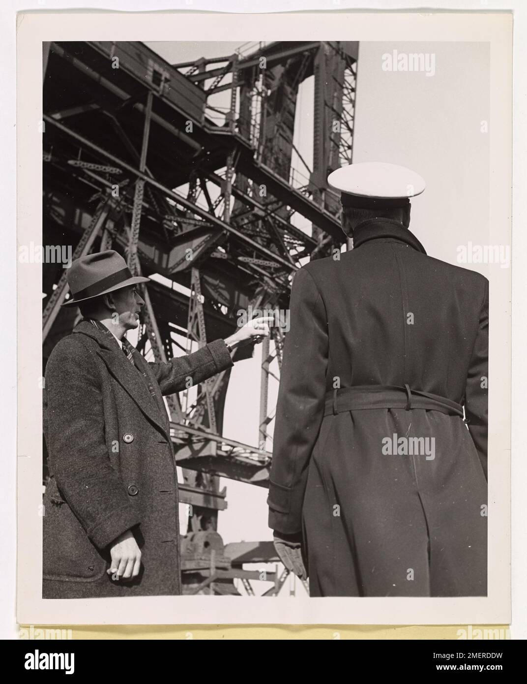 Sgt. O'Donnell von der Reading Company Polizei wird mit einem Freiwilligen Port Security Force Offizier aus Philadelphia gezeigt, der die Ausrüstung in einer Hafenanlage bespricht. Im Hintergrund ist eine große Struktur sichtbar, die für das Verladen von Schiffen verwendet wird und die Bedeutung der Hafensicherheit und -Logistik während des Kriegsbetriebs unterstreicht. Stockfoto