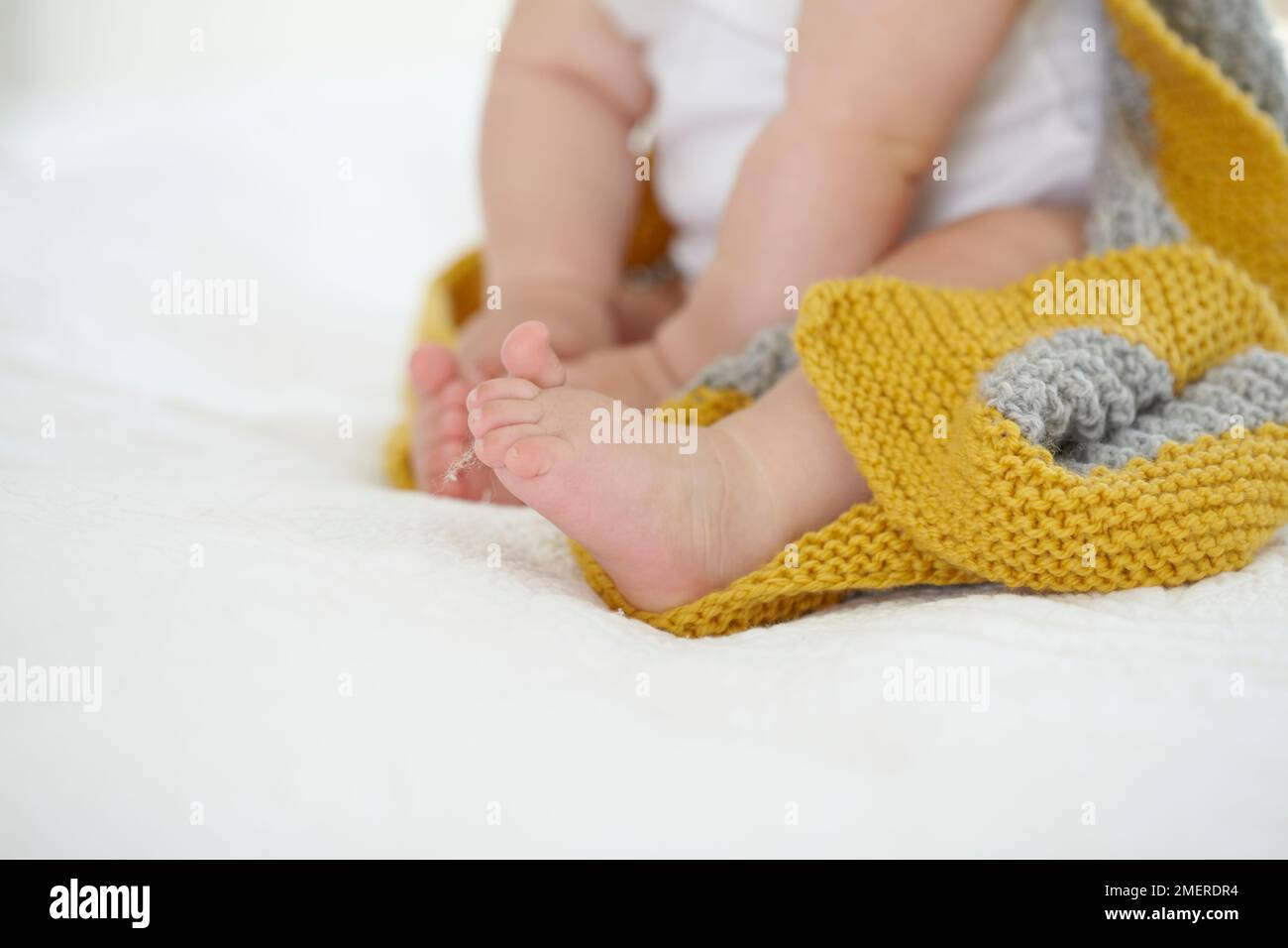 Ein kleines Mädchen, das im Bett sitzt, eine gestrickte Kapuzendecke trägt, 9 Monate Stockfoto