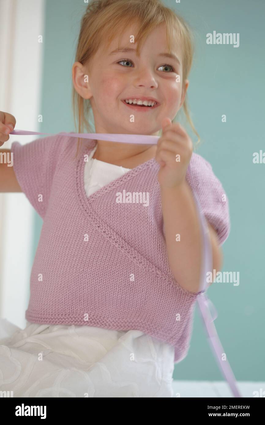 Ein Mädchen trägt einen weißen Rock und eine pinkfarbene Strickjacke, 4 Jahre Stockfoto