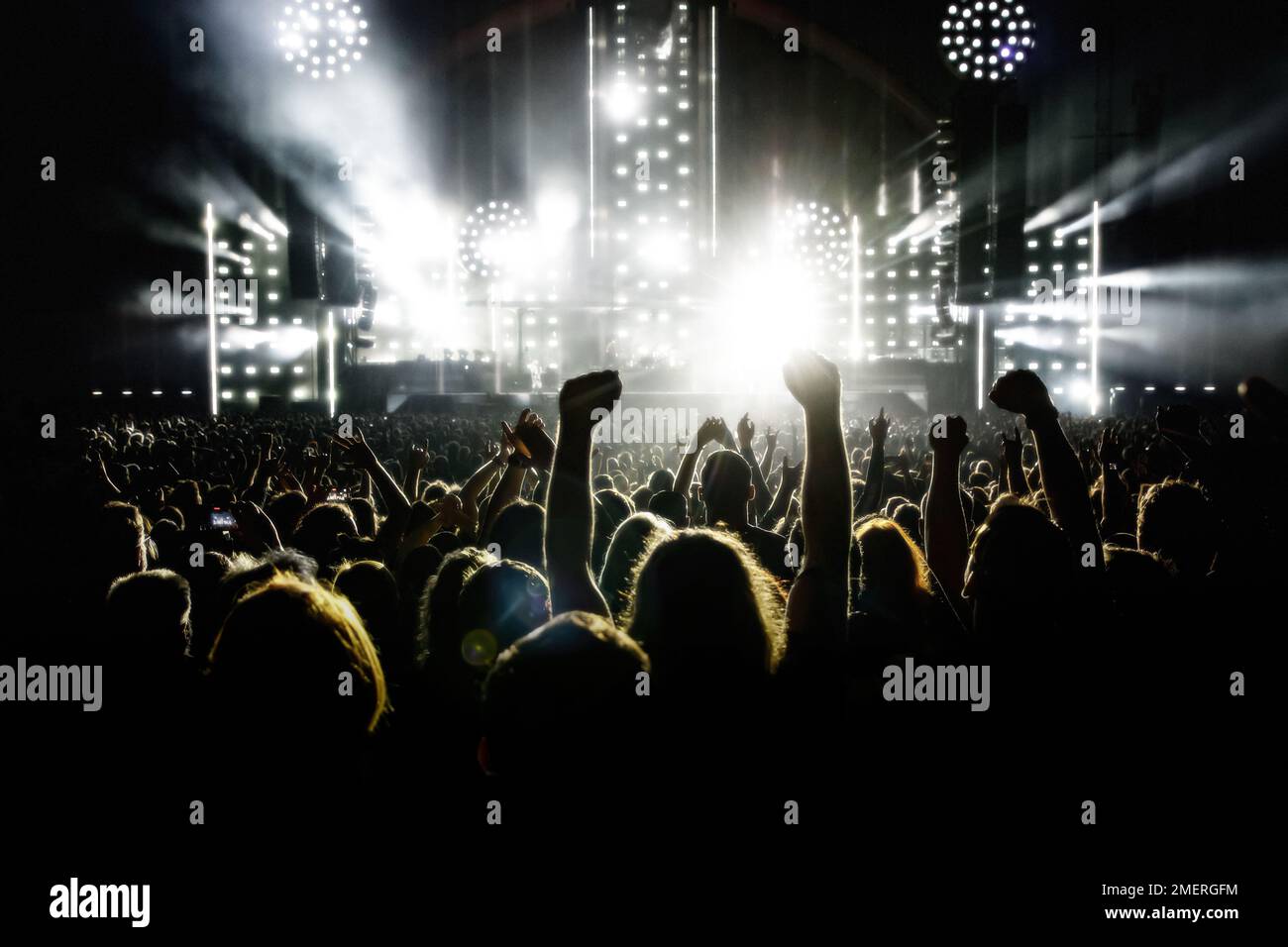 Eine Menge Leute mit erhobenen Armen während eines Musikkonzerns mit einer fantastischen Lichtshow. Schwarze Silhouetten. Stockfoto