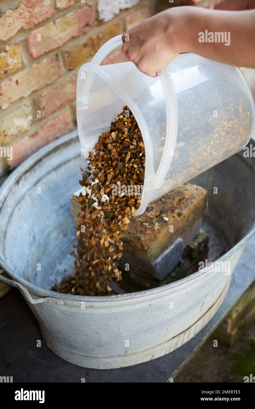 Befüllung eines alten, galvanisierten Stahlbades mit Steinen zur Entwässerung Stockfoto