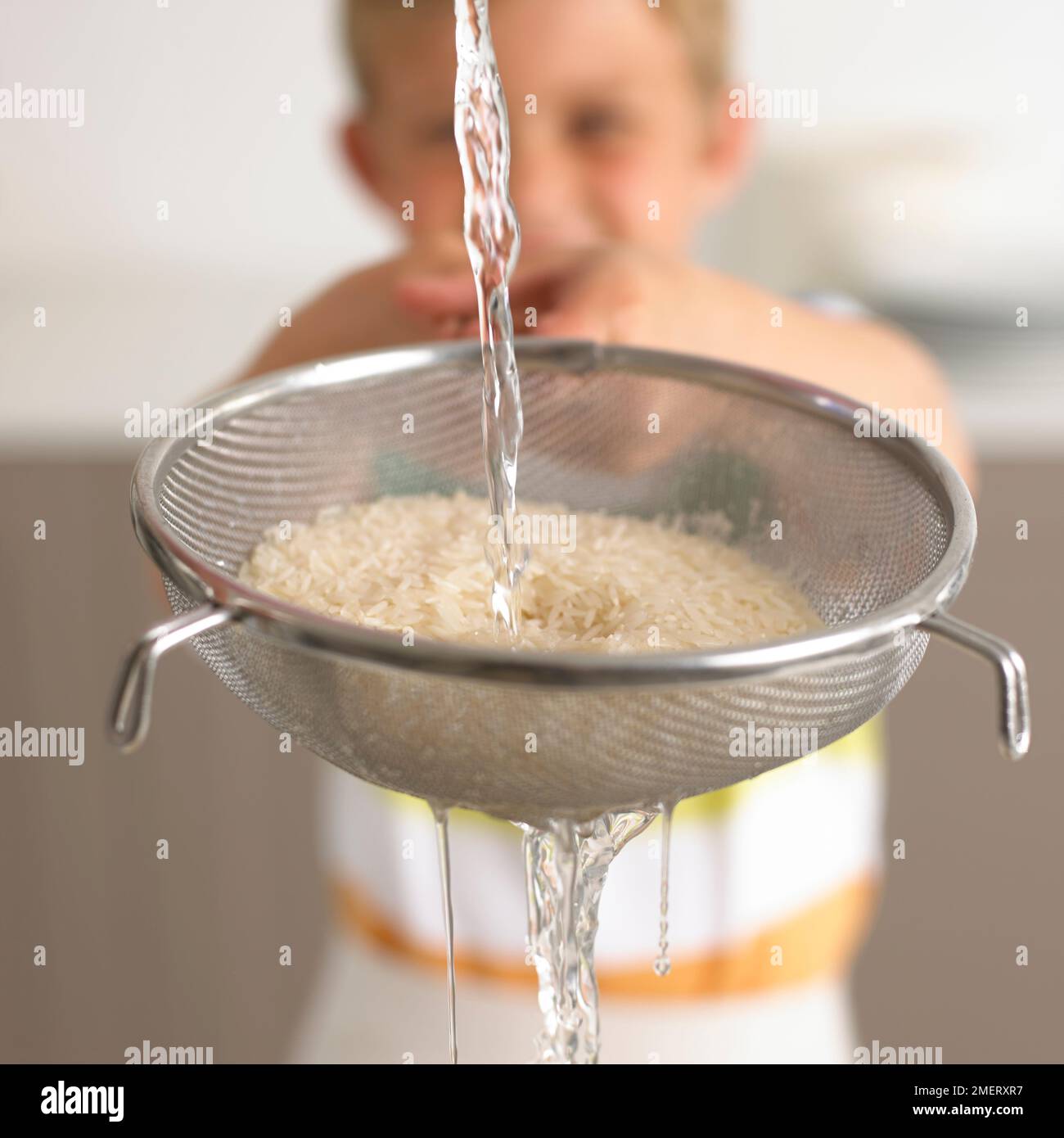 Reis in einem Sieb Waschen mit Wasser, 6 Jahre Stockfoto