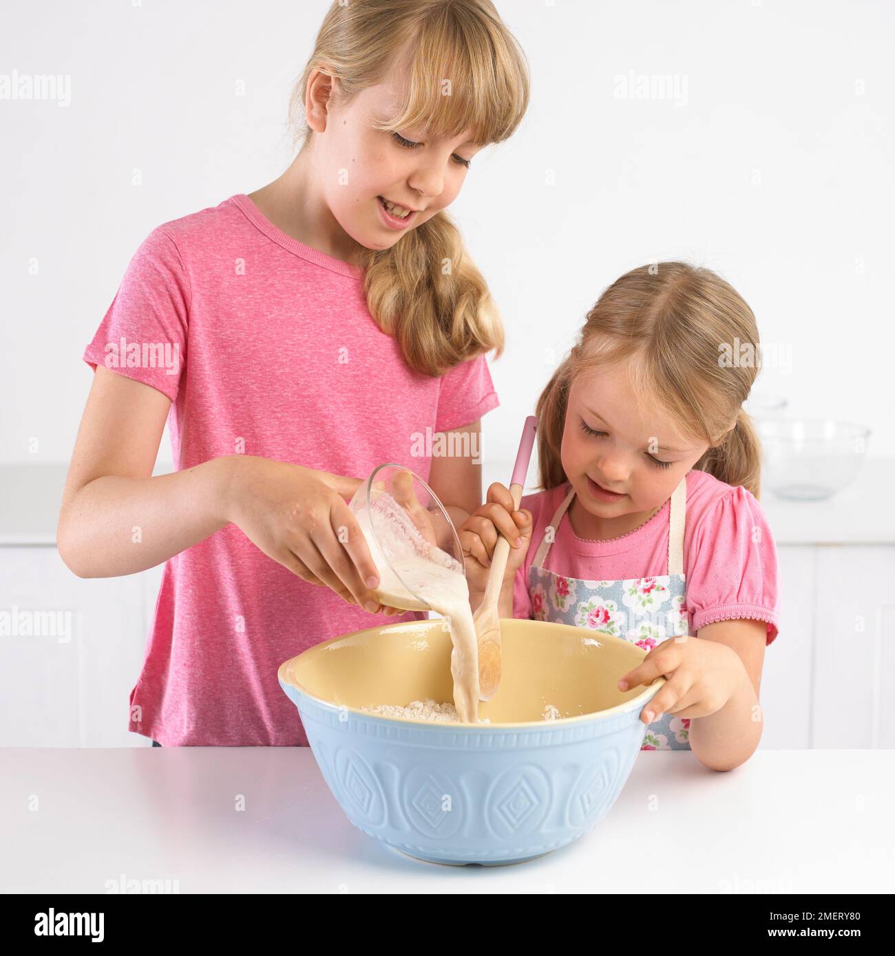 Mädchen gießen Hefe und Wasser Mischung in die Schüssel mit Mehl, 5 Jahre und 9 Jahre Stockfoto