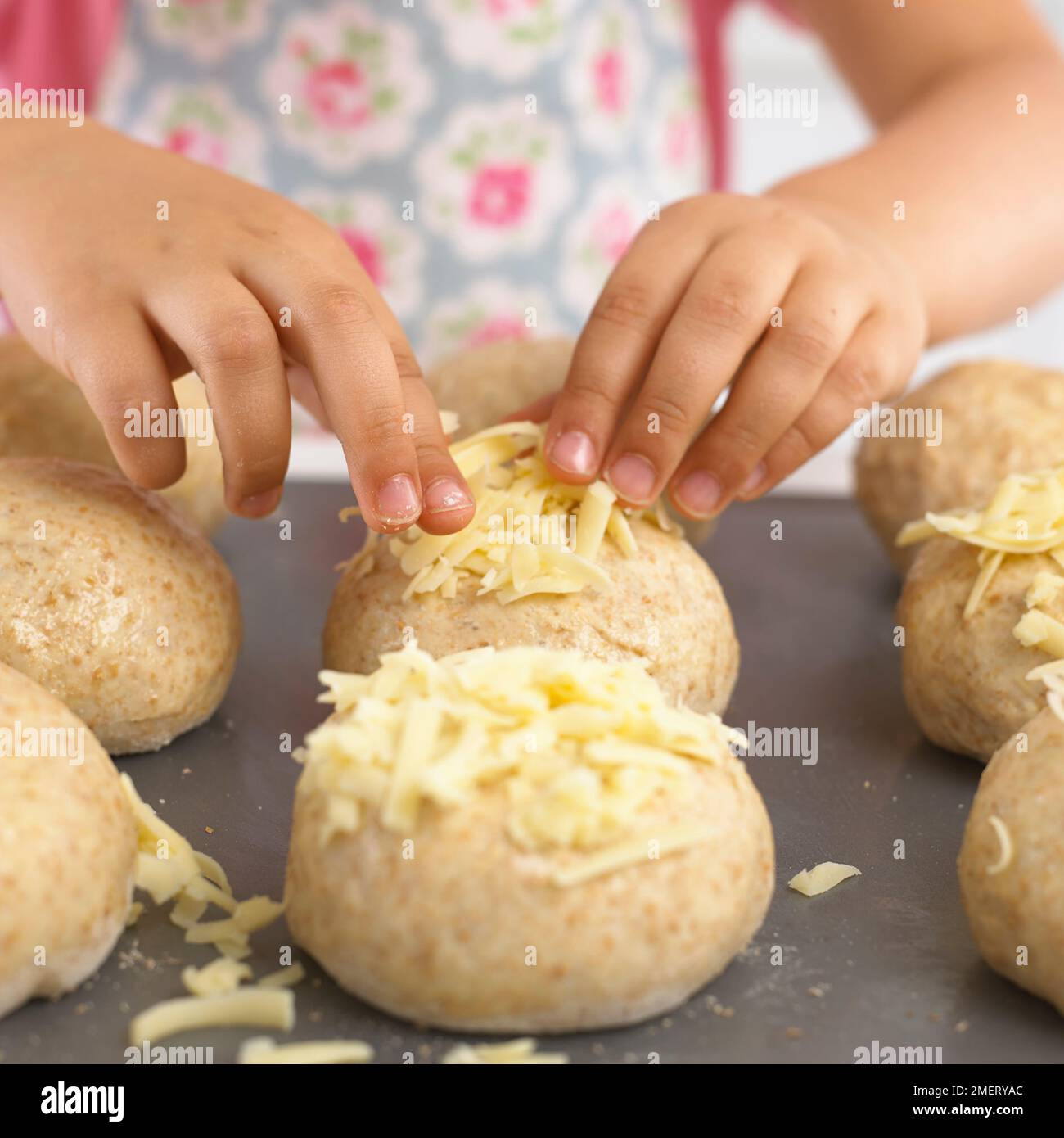 Pressen von geriebenem Käse auf ungekochte Brötchen Stockfoto