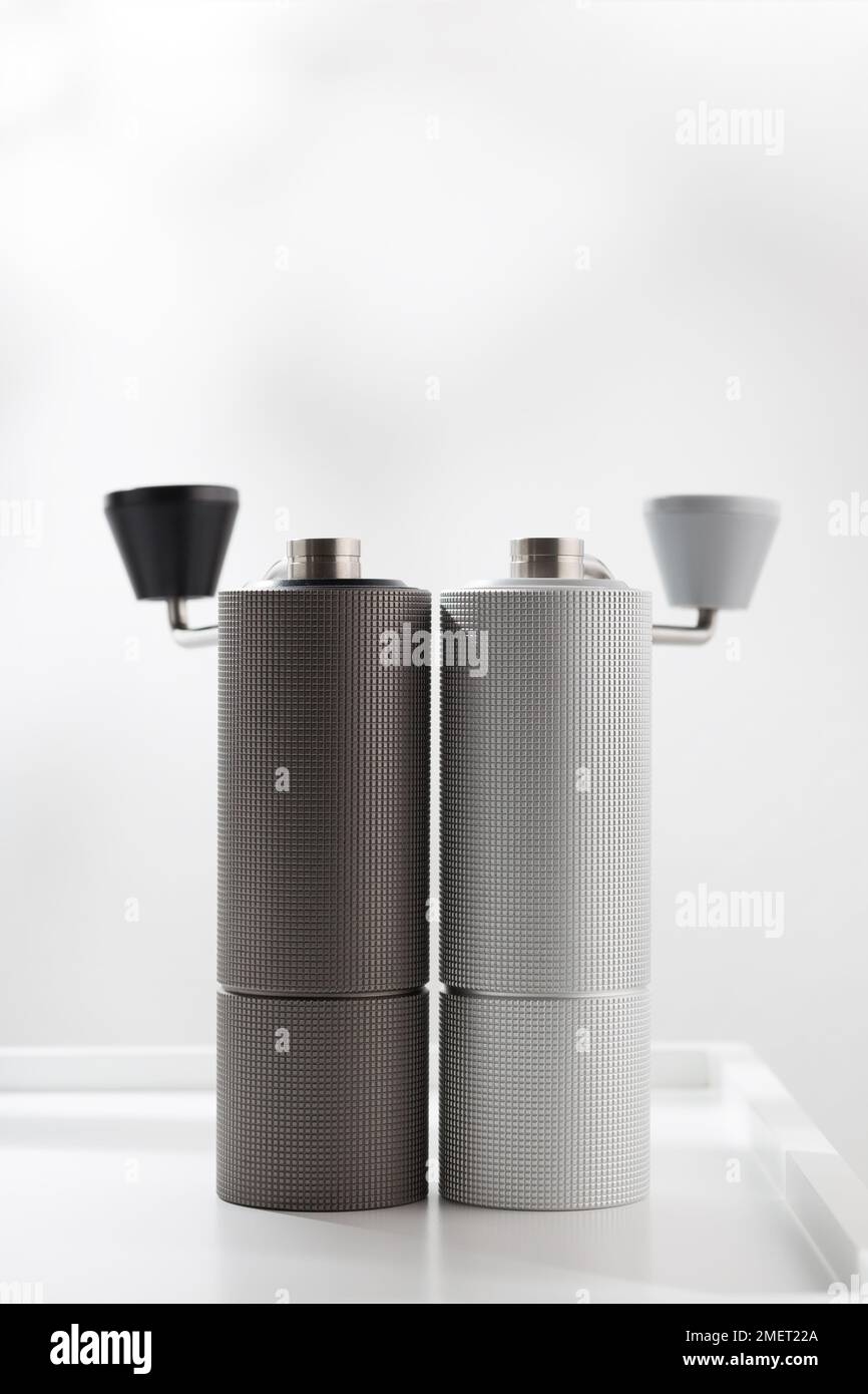 Vertikales Foto der manuellen Kaffeemühle in Hellgrau und Dunkelgrau auf dem weißen Tisch. Stockfoto