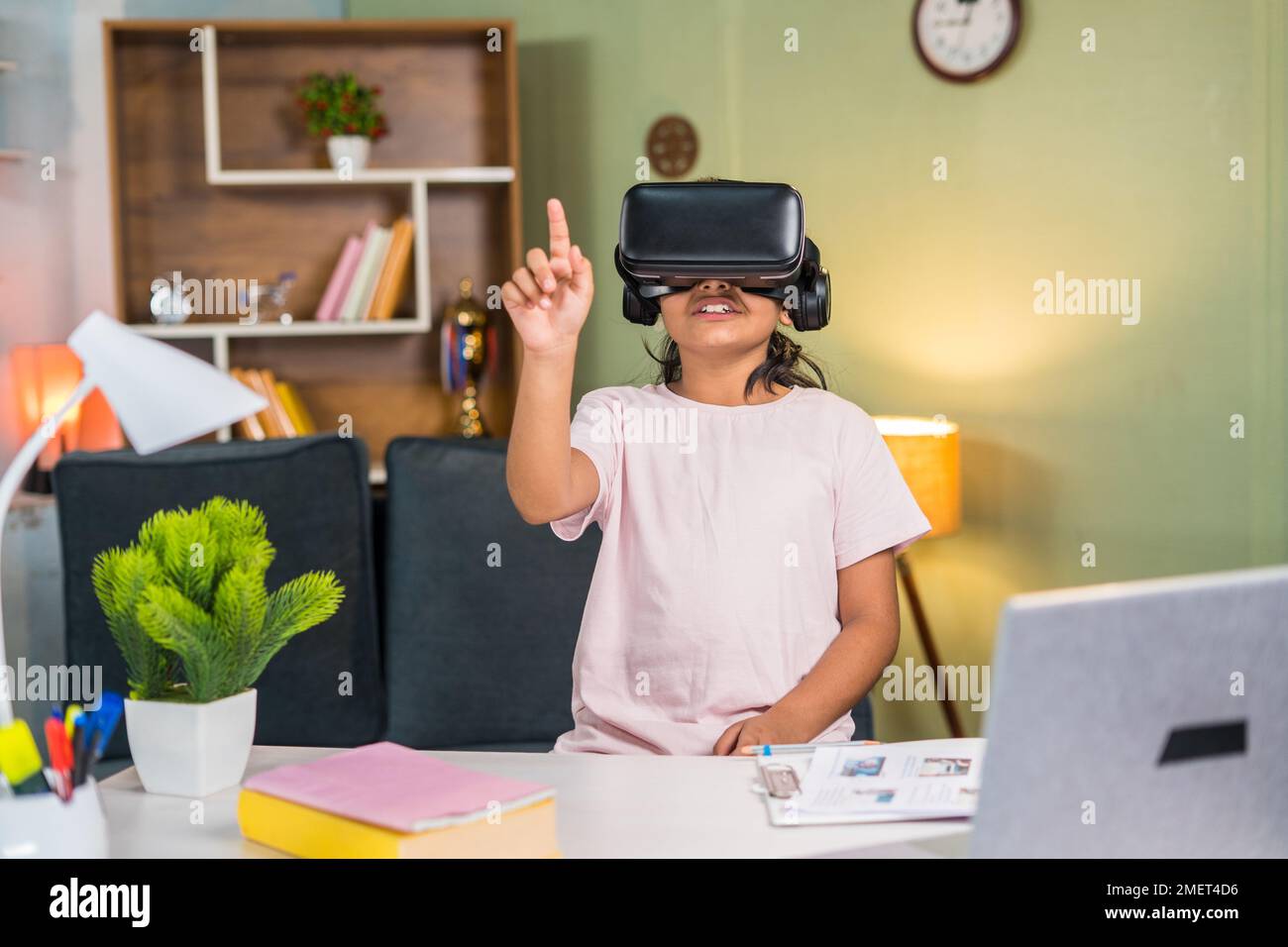 Mädchen mit VR oder virtuellem Hörer, die zu Hause online oder virtuell vor dem Studientisch zuhören – Vorstellung von moderner Bildung, Lernen und Stockfoto