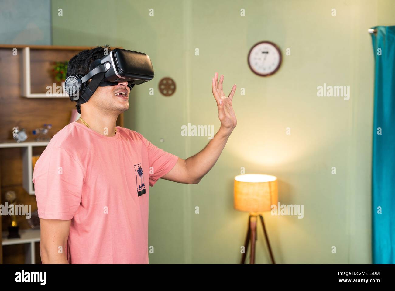 Junger Mann, der beim Online-Treffen in der metaversen oder virutalen Welt Hand winkt, indem er ein Virtual-Reality- oder VR-Headset trägt – Konzept von futuristischer Technologie Stockfoto