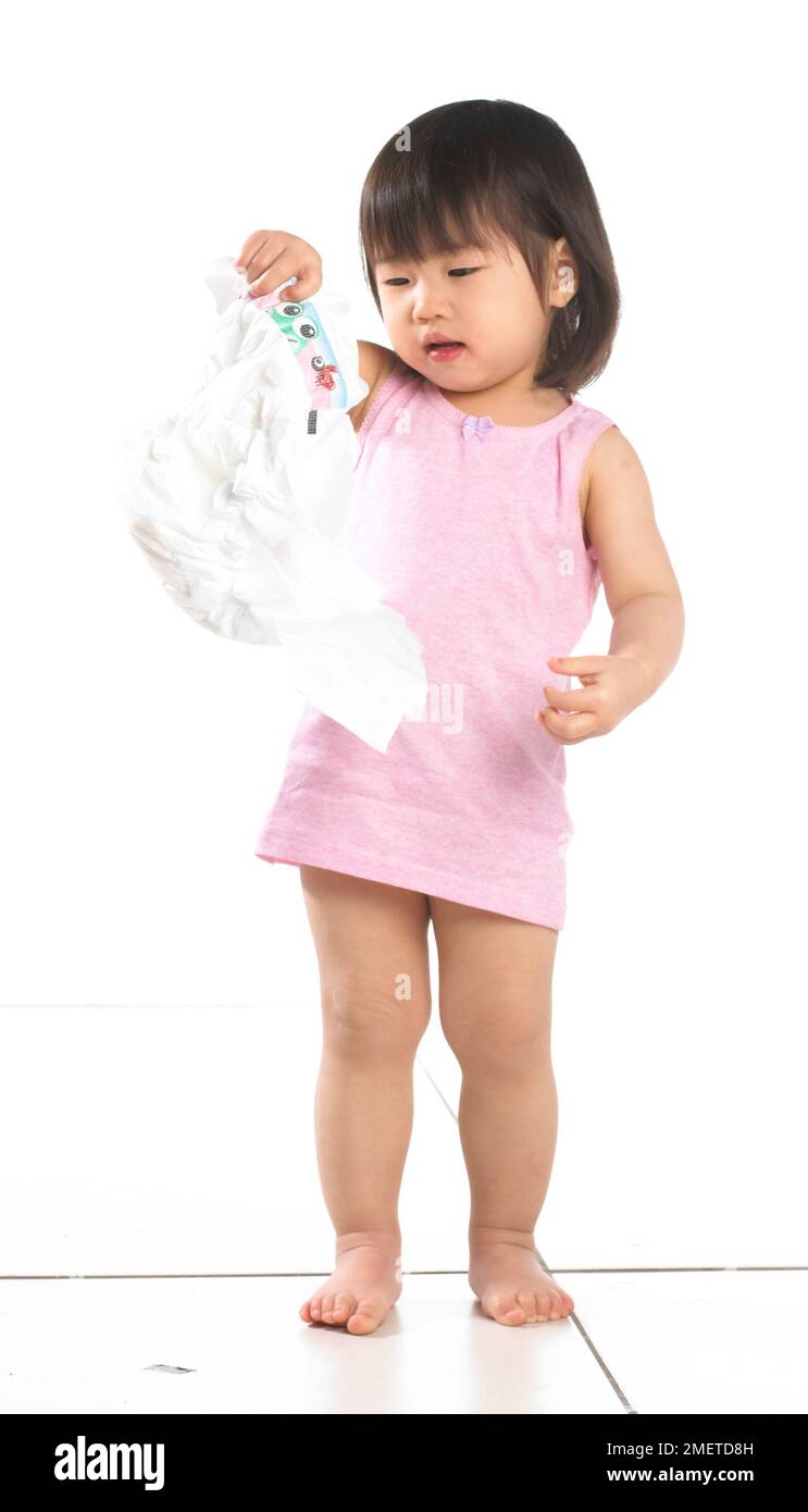 Ein Mädchen, das in einer pinken Weste steht und eine Windel hält, 20 Monate Stockfoto