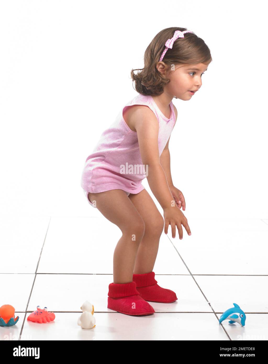 Mädchen mit Weste, Hosen und Hausschuhen, die sich auf dem Boden zu Spielzeug beugen, 20 Monate Stockfoto