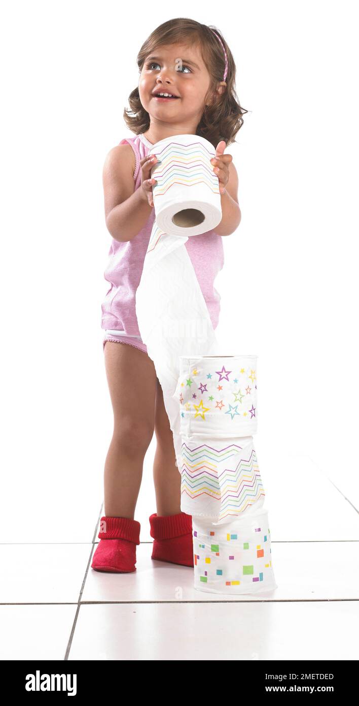 Mädchen mit Weste, Hosen und Hausschuhen, die einen Turm aus Toilettenpapierrollen machen, 20 Monate Stockfoto