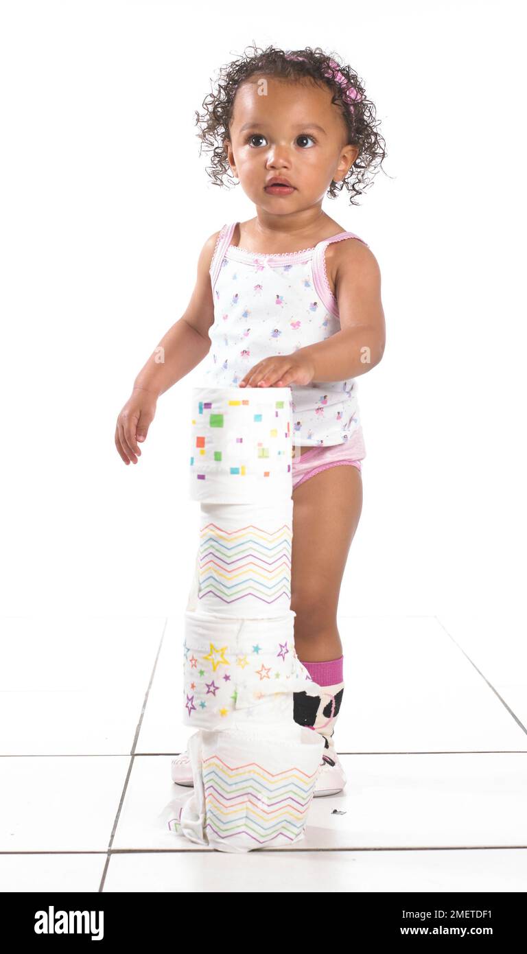 Mädchen mit Weste, Hosen und Hausschuhen, stapelbare Toilettenpapierrollen, 16 Monate Stockfoto