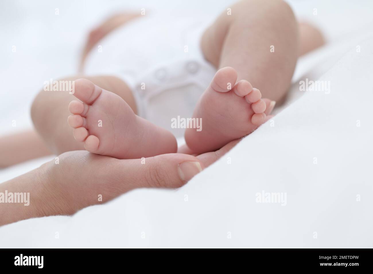 Frauenhand, die Füße eines kleinen Mädchens hält (6 Wochen) Stockfoto