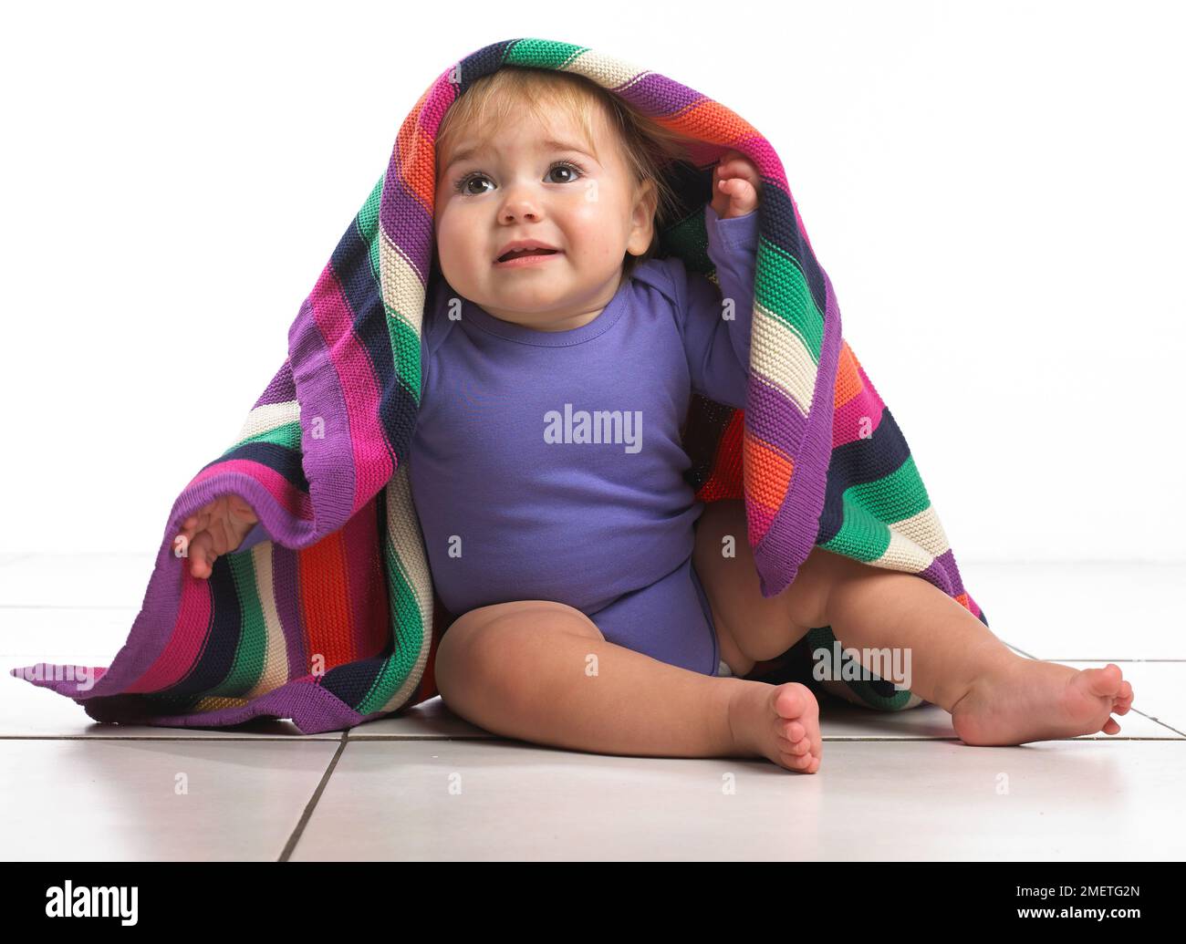 Babymädchen (12 Monate) mit bunt gestreifte Decke auf den Kopf Stockfoto