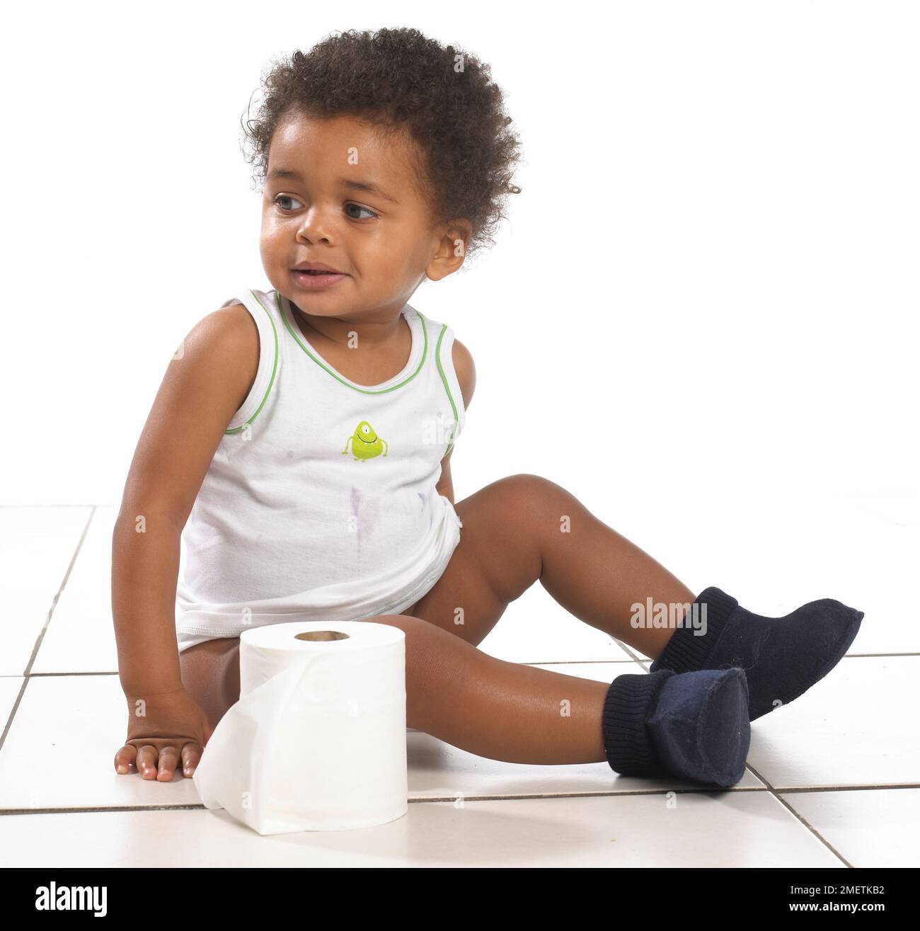 Ein Junge mit Weste und Hausschuhen, der auf dem Boden sitzt, mit einer Rolle Toilettenpapier, 17 Monate Stockfoto
