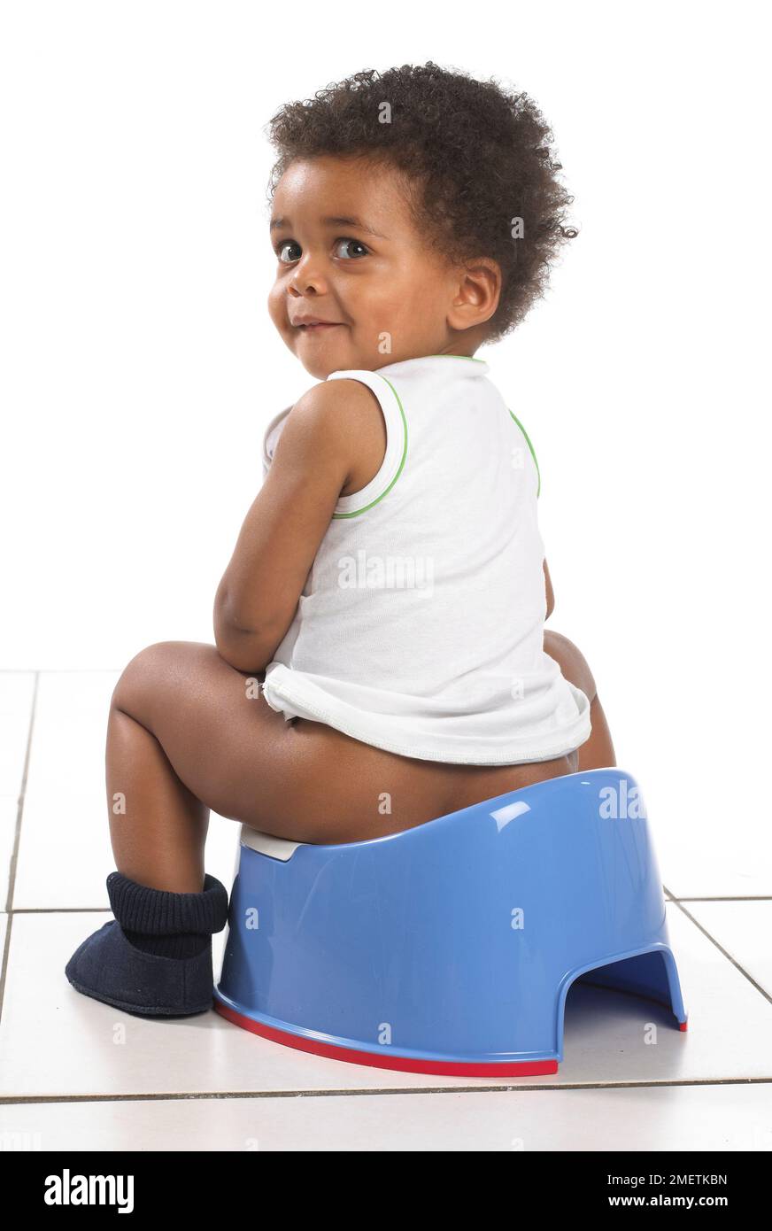 Ein Junge mit Weste und Hausschuhen sitzt auf einem blauen Töpfchen, 17 Monate Stockfoto