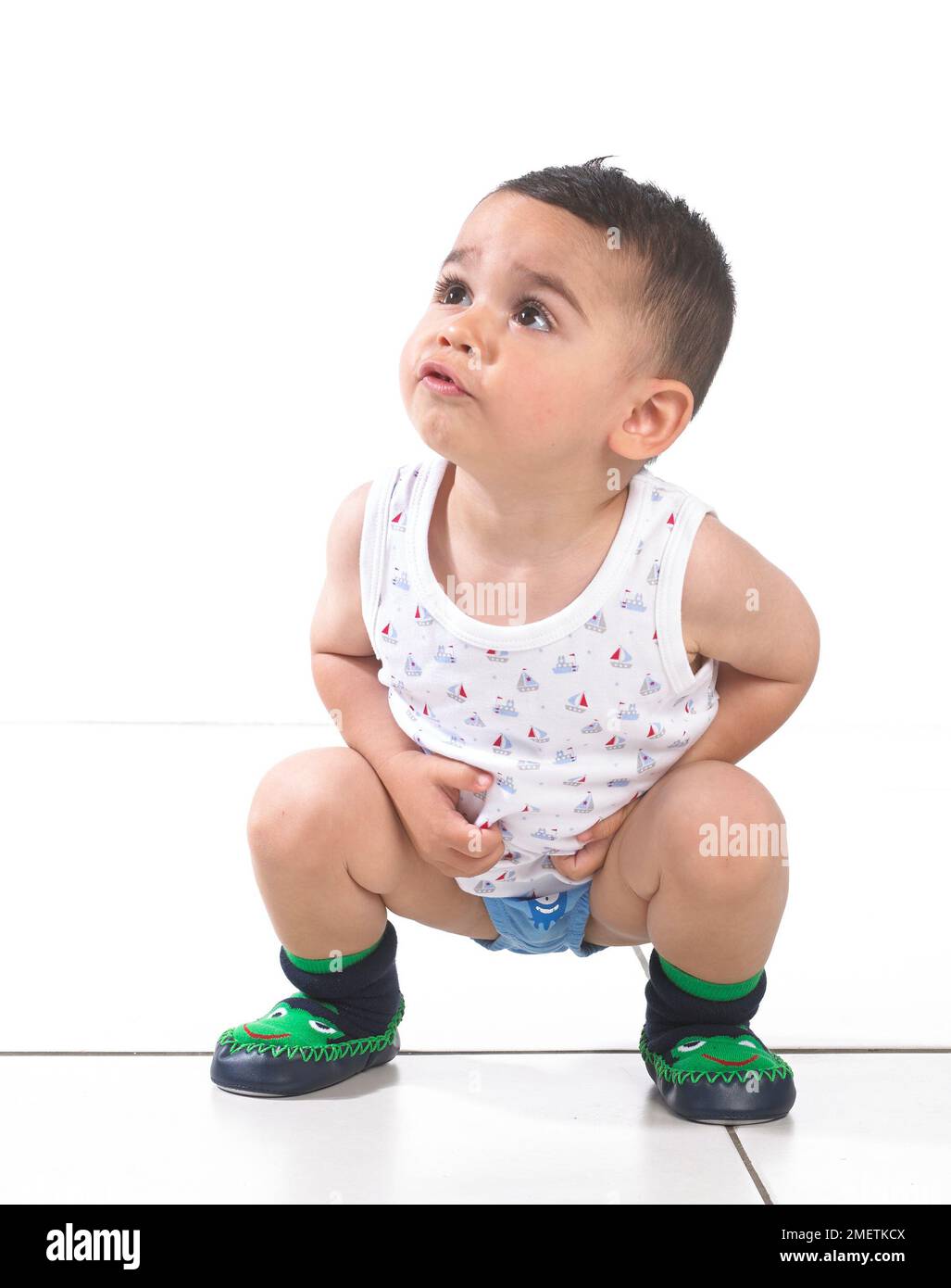 Ein Junge mit Weste, Hosen und Hausschuhen, in der Hocke, 15 Monate Stockfoto